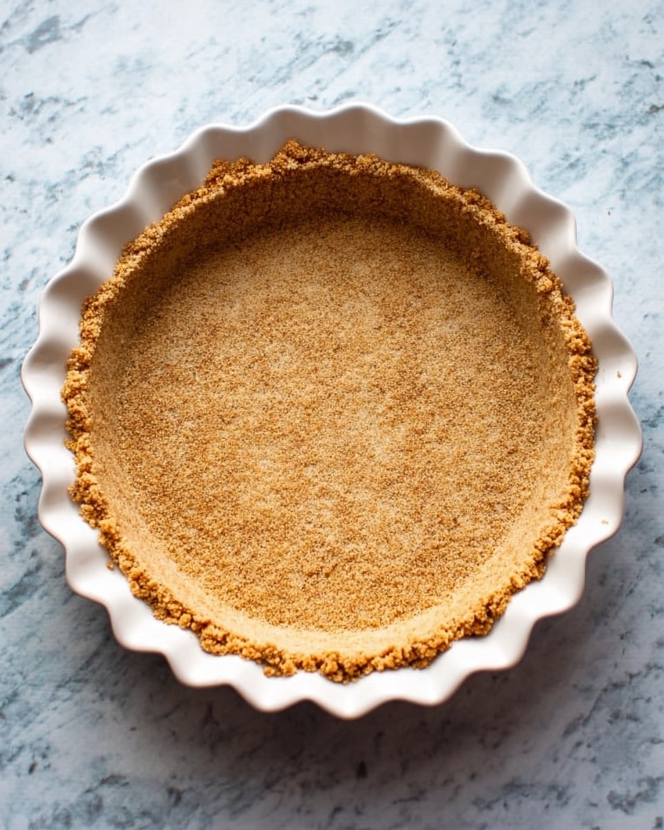 A white pie dish with scalloped edges holds a single layer of golden-brown crumb crust pressed evenly along the bottom and sides, creating a rough textured shell ready to be filled, all placed on a white marbled surface photo taken with an iphone --ar 4:5 --v 7