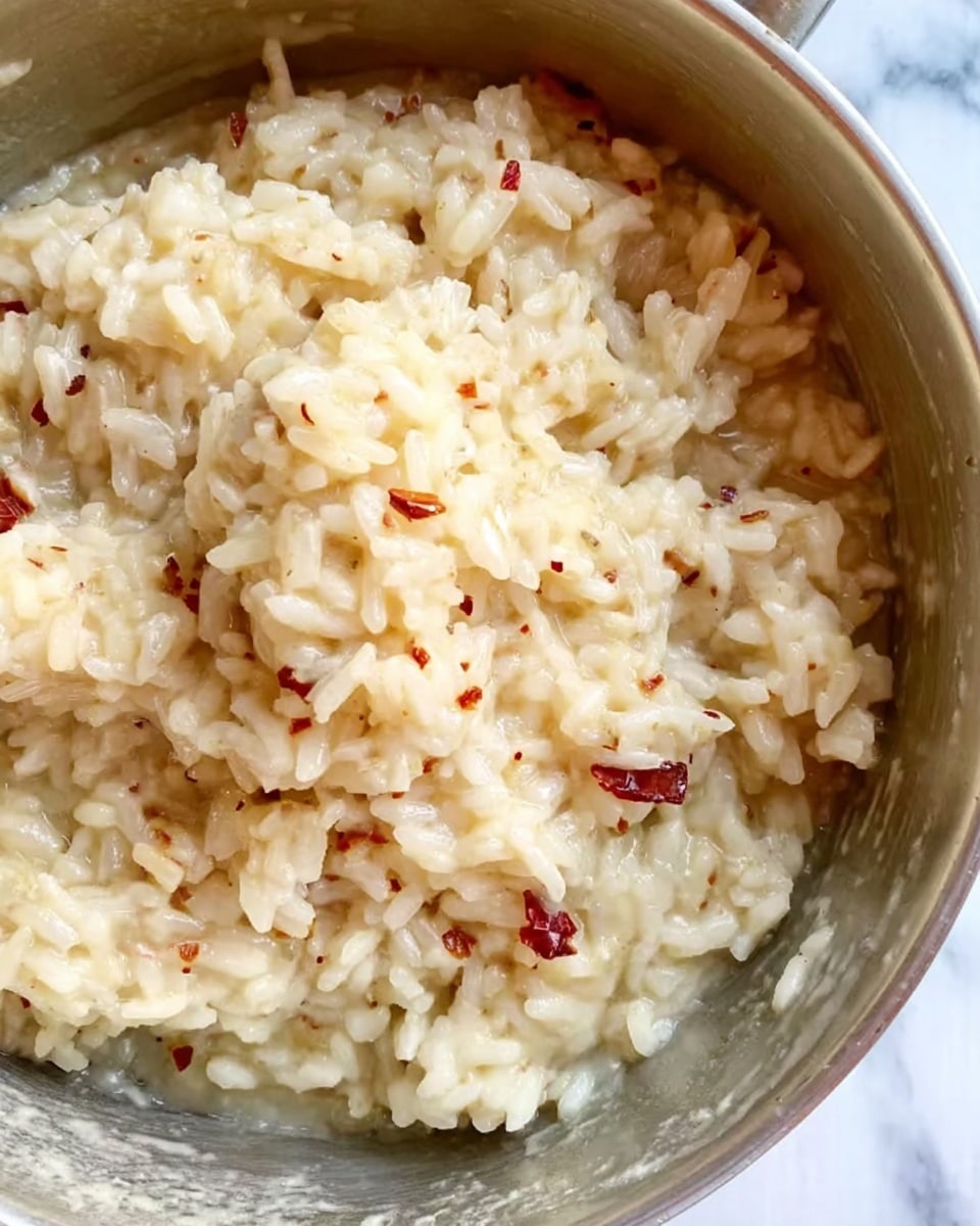 A white bowl filled with creamy beige oatmeal, with a soft and slightly lumpy texture, topped in the center with four thin, red-skinned apple slices arranged in a fan shape. A silver spoon rests inside the bowl on the right side, partially submerged in the oatmeal. The bowl is placed on a white marbled surface, with two whole red apples visible in the top left corner and a small glass jar containing light brown sugar in the top right corner. A piece of blue cloth with frayed edges is in the bottom left corner. photo taken with an iphone --ar 4:5 --v 7