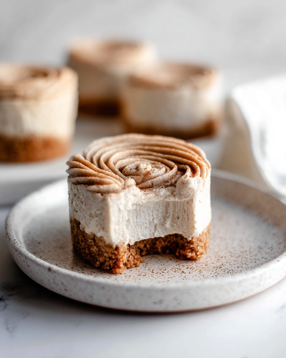 A black speckled muffin tray with white paper liners holds nine round portions of two layers: a crumbly light brown base layer of crushed biscuits filling the bottom of each liner, and a smooth, creamy, light beige mixture filling the top four liners, swirled gently on the surface. The tray is placed on a white marbled surface, creating a clean contrast with the dark tray and light contents. Photo taken with an iphone --ar 4:5 --v 7