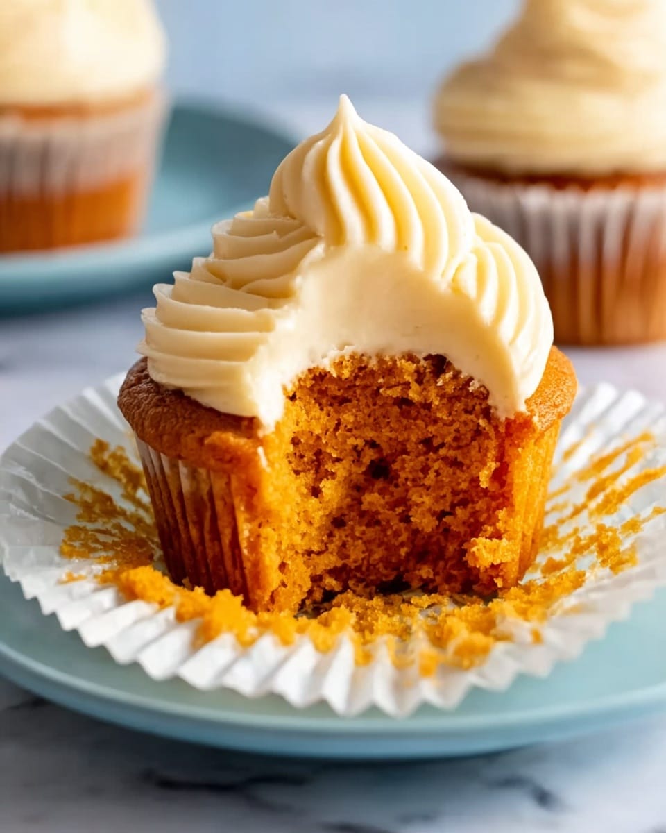 A dark gray muffin tray holds twelve white paper liners filled with smooth orange batter that is evenly swirled on top. The tray sits on a white marbled surface, with a metal spatula resting nearby, coated in the same orange batter. The lighting highlights the creamy texture and warm color of the batter, ready to be baked photo taken with an iphone --ar 4:5 --v 7
