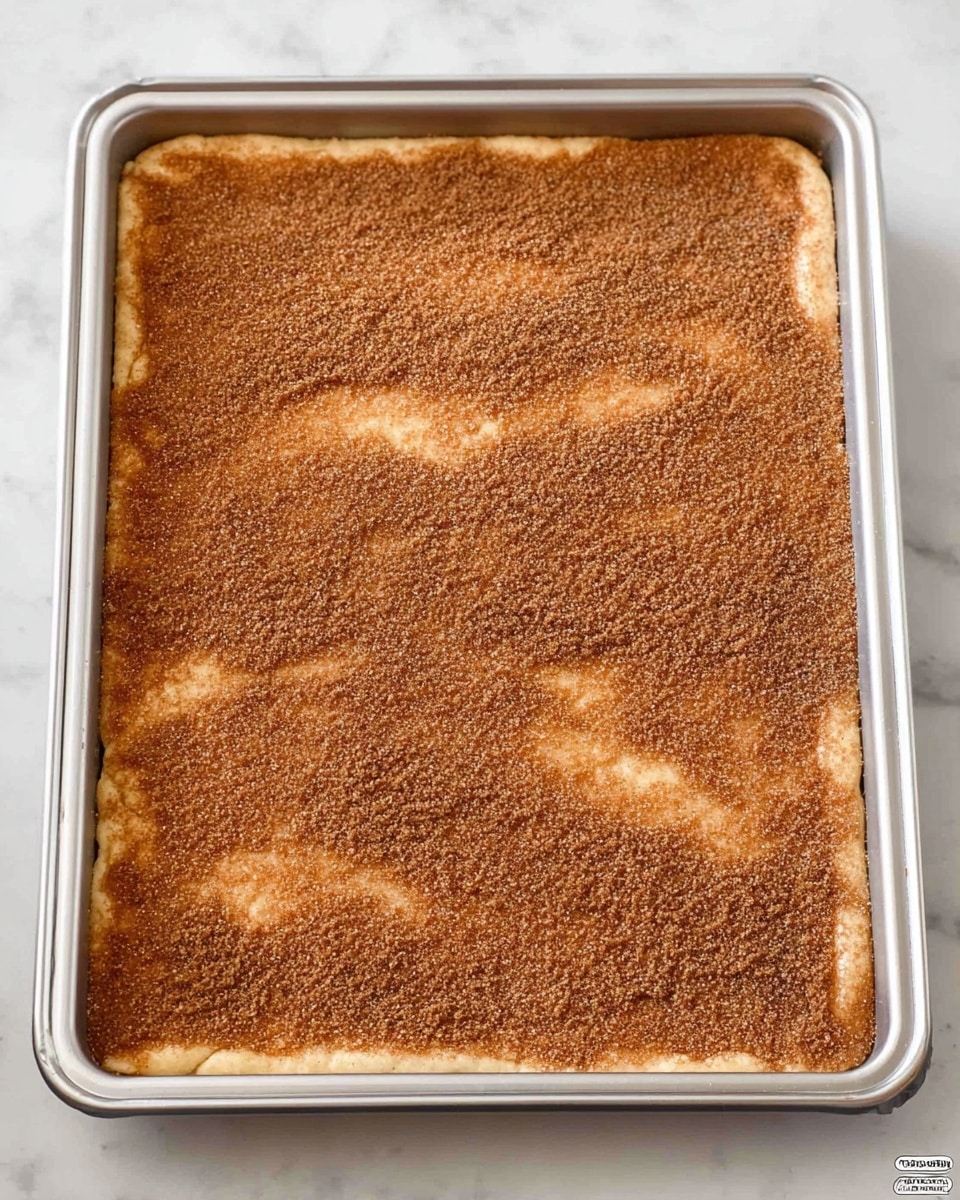A stack of five layered square pieces shows a close-up view, each piece having three visible layers: a thin, light brown crispy base with a rough texture, a smooth middle layer of creamy white filling, and a top layer covered in a fine dusting of cinnamon sugar giving it a slightly grainy brown surface. The pieces are uneven and some edges are slightly broken, highlighting the crispy texture. The background is a white marbled surface. photo taken with an iphone --ar 4:5 --v 7