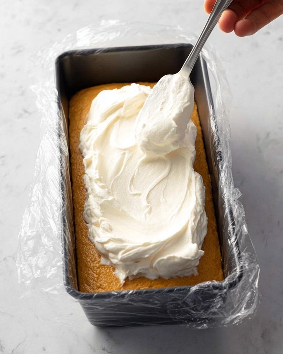 A slice of layered dessert is shown on a white plate with a silver spoon and a brown-handled knife resting on the plate edge. The dessert has three main layers: the bottom layer consists of round, light brown biscuit pieces tightly packed side by side; the middle layer is a thick, creamy, yellowish filling; the top layer is a fluffy white cream dusted lightly with cocoa powder. The background has a colorful cloth with a blue, red, and yellow leaf pattern, and the edge of another white plate with a dessert piece is visible. The photo taken with an iphone --ar 4:5 --v 7