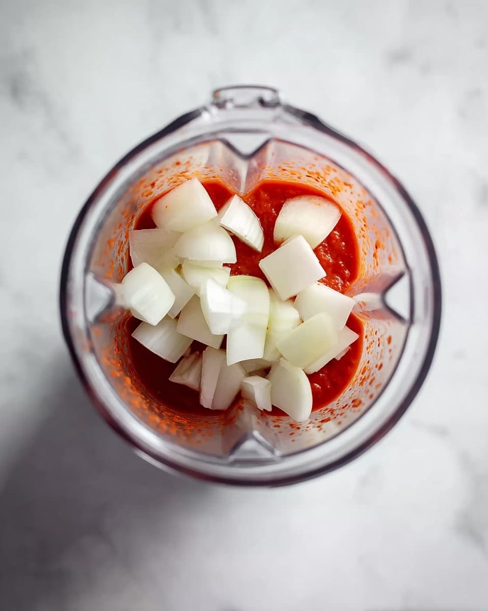 A white bowl filled with orange-red noodles mixed in a thick sauce, topped with small green herb leaves front and center, placed on a white marbled surface. Behind it, a teal pot containing more of the same noodle mixture with a wooden spoon resting inside, with noodles and sauce visible on the spoon. photo taken with an iphone --ar 4:5 --v 7