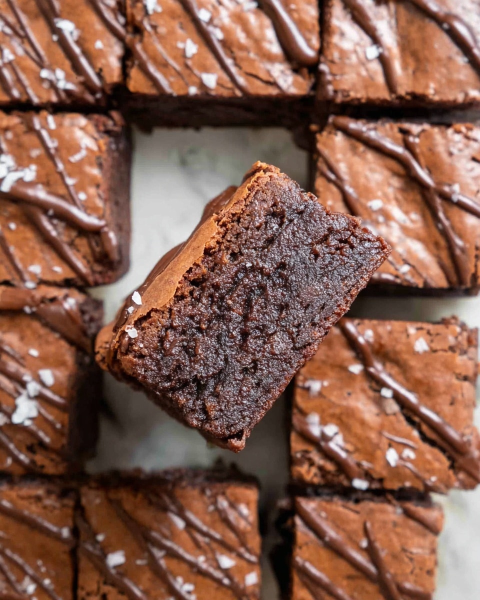 A close-up of a square brownie piece lifted above a group of cut square brownies arranged closely together on a white marbled surface. The brownies have a dark brown, slightly rough and moist texture inside with a shiny, slightly cracked light brown top layer. There are smooth chocolate drizzles on the top of all brownies, along with small white flakes sprinkled around. The lifted brownie is held by a woman's hand from the top side. photo taken with an iphone --ar 4:5 --v 7