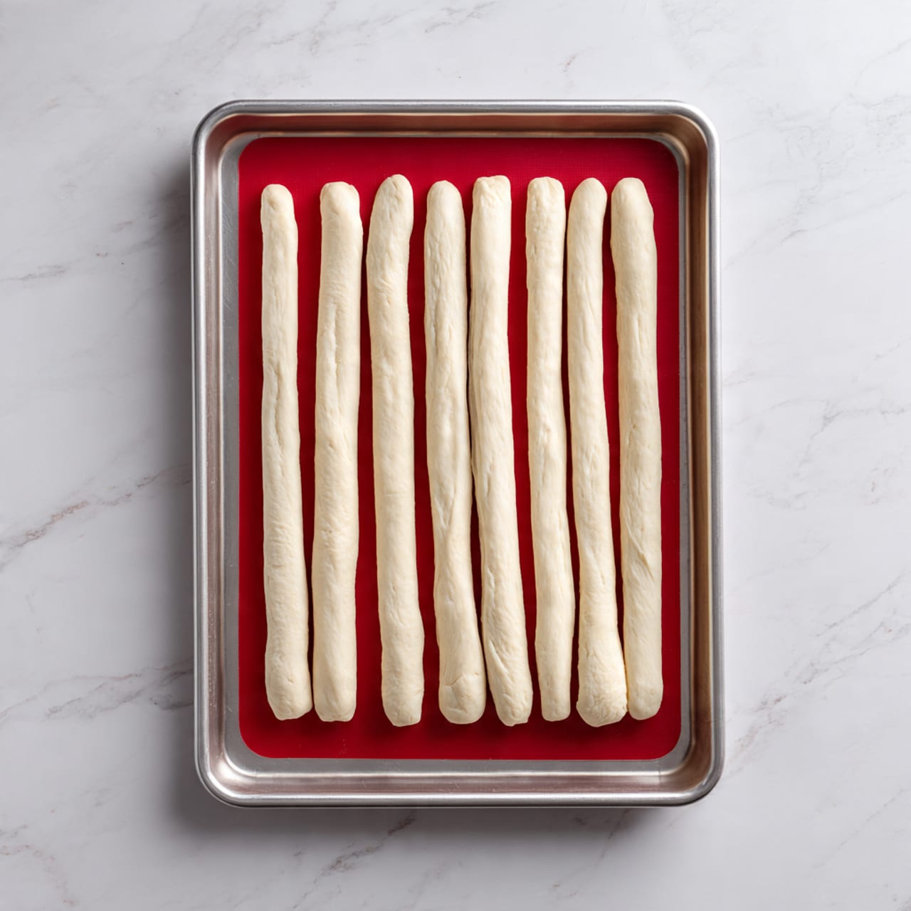 A close-up view of a pile of golden brown breadsticks with a shiny surface and light herb specks, stacked on a red and white checked cloth on top of a wooden board. One breadstick on top has a bite taken out, showing a soft, white, fluffy interior. On the left edge, a small part of a white bowl with bright red marinara sauce is visible, and on the right edge, a glimpse of a bowl with green lettuce leaves can be seen. The scene sits on a white marbled surface. photo taken with an iphone --ar 4:5 --v 7