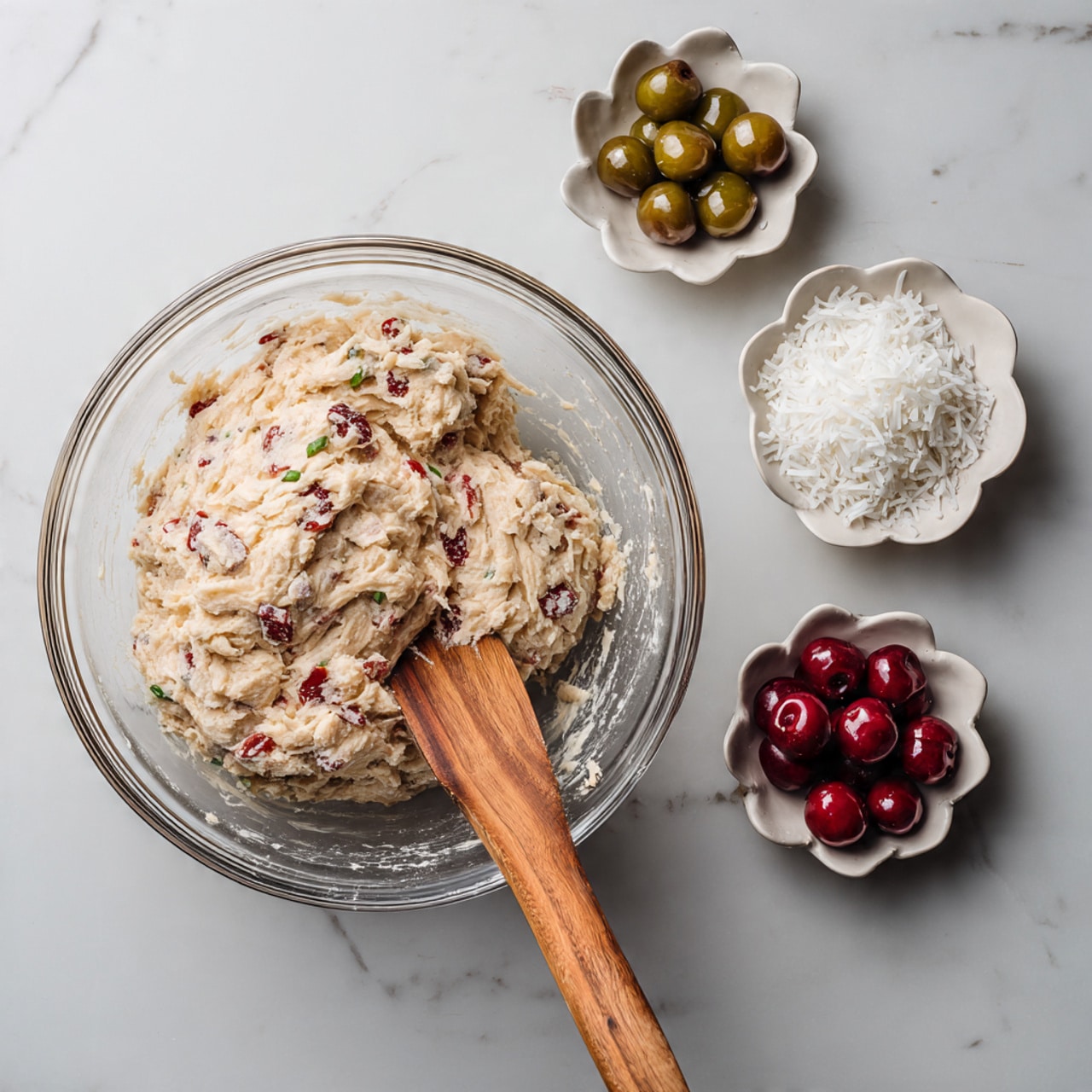 A white plate with around twelve round cookies piled on top of each other is shown. Each cookie has a light beige color mixed with small red and green bits inside, showing textured pieces of fruit. There are about five thin, light cream-colored stripes of drizzle running diagonally across the cookies. Small white shredded flakes are sprinkled over the cookies, adding another texture. The plate sits on a white marbled texture. photo taken with an iphone --ar 4:5 --v 7
