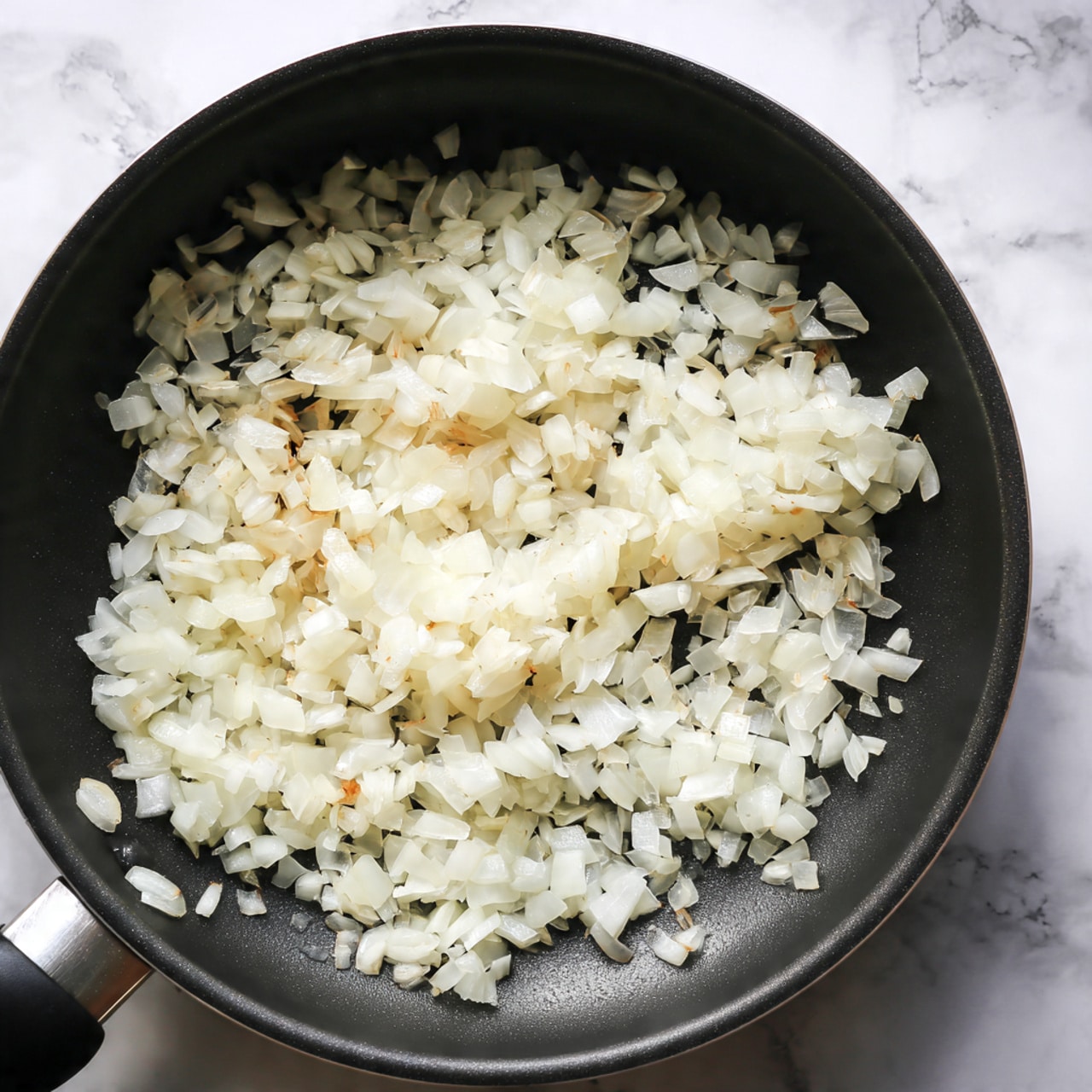 A close-up view of a black pan filled with small, white, diced onions cooking evenly across the surface. The onions are slightly shiny, indicating they are being gently cooked with a little oil, spreading out in a single layer inside the pan. The pan is black and smooth, with a visible handle on the left side. The background is changed to a white marbled texture. photo taken with an iphone --ar 4:5 --v 7