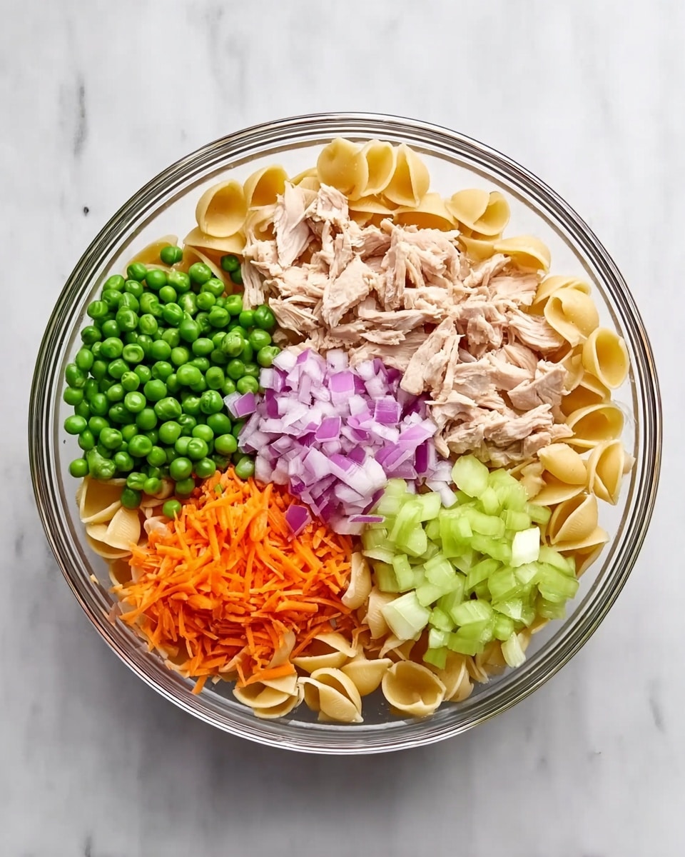 The image shows a clear glass bowl filled with six different groups of ingredients arranged on top of small pasta shells. At the top right, there are beige pieces of cooked chicken. At the top left, there are bright green peas. Just below the peas, there are finely chopped red onions in a light purple shade. Below the onions, shredded orange carrots are placed. To the right of the carrots, there are diced light green celery pieces. All these ingredients rest on a bed of beige pasta shells. The bowl is placed on a white marbled surface. photo taken with an iphone --ar 4:5 --v 7