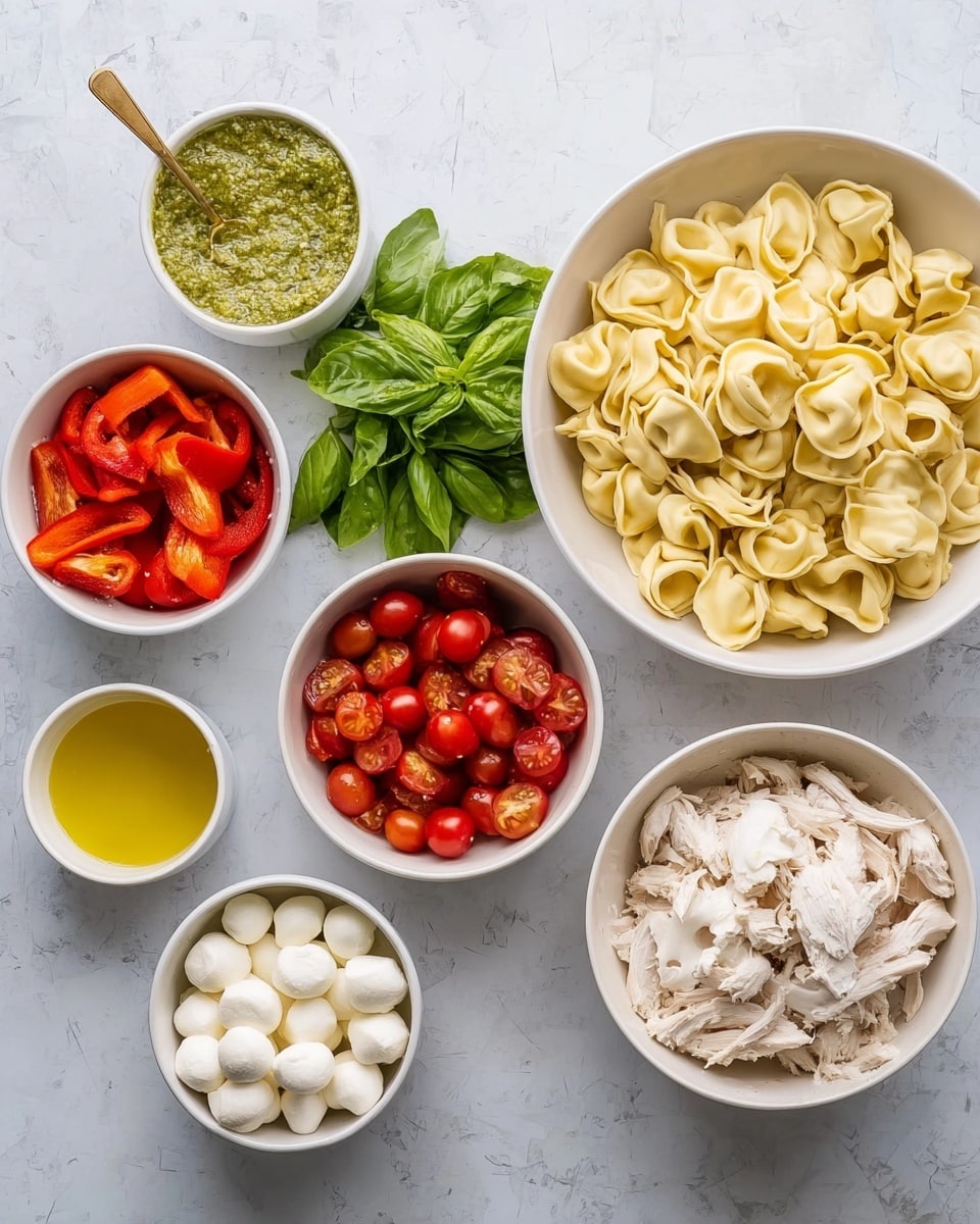 Seven white bowls arranged on a white marbled surface hold different food items. The largest bowl on the right is full of cooked tortellini pasta, which is a pale yellow color with a smooth texture. Below it, there is a bunch of fresh green basil leaves. To the left of the tortellini, there is a small white bowl of light green pesto with a small gold spoon inside. Below the pesto, a small white bowl contains light yellow olive oil. Moving left, a bowl with bright red roasted bell peppers, another bowl with halved cherry tomatoes showing juicy red and green inside, a bowl filled with small white mozzarella balls, and at the far left, shredded white chicken pieces fill a larger white bowl. The white marbled surface clearly shows beneath the bowls. The photo is taken with an iphone --ar 4:5 --v 7