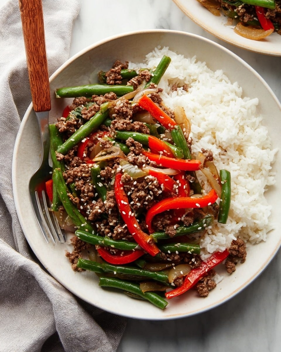 A white pan filled with a colorful stir-fry showing three main layers: at the bottom, cooked ground meat in small brown crumbles; on top of that, bright green beans cut into short pieces; and scattered red bell pepper slices along with translucent cooked onion strips. The dish is sprinkled with small white sesame seeds and has a wooden spoon resting on the left side inside the pan. The pan is placed on a crumpled gray cloth on a white marbled surface, with a small white bowl containing sesame seeds next to it. photo taken with an iphone --ar 4:5 --v 7