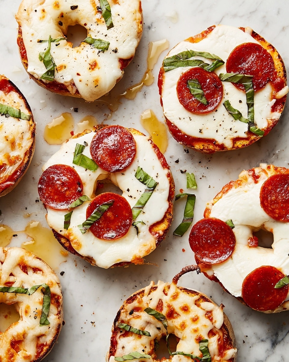The image shows several mini pizzas made on bagel halves placed on a white marbled surface. Each pizza has a base layer of melted white cheese with a smooth and slightly browned texture on top. Some bagels have a thin red tomato sauce layer underneath the cheese, visible near the edges. The pizzas are garnished with small pieces of fresh green basil leaves scattered on top. One pizza has three round slices of pepperoni with a shiny reddish-brown color sitting on the white cheese. There are some droplets of golden oil around the pizzas, adding shine and a slight greasy look. The bagels have a light golden-brown toasted crust with a soft inside visible through the hole in the center. photo taken with an iphone --ar 4:5 --v 7