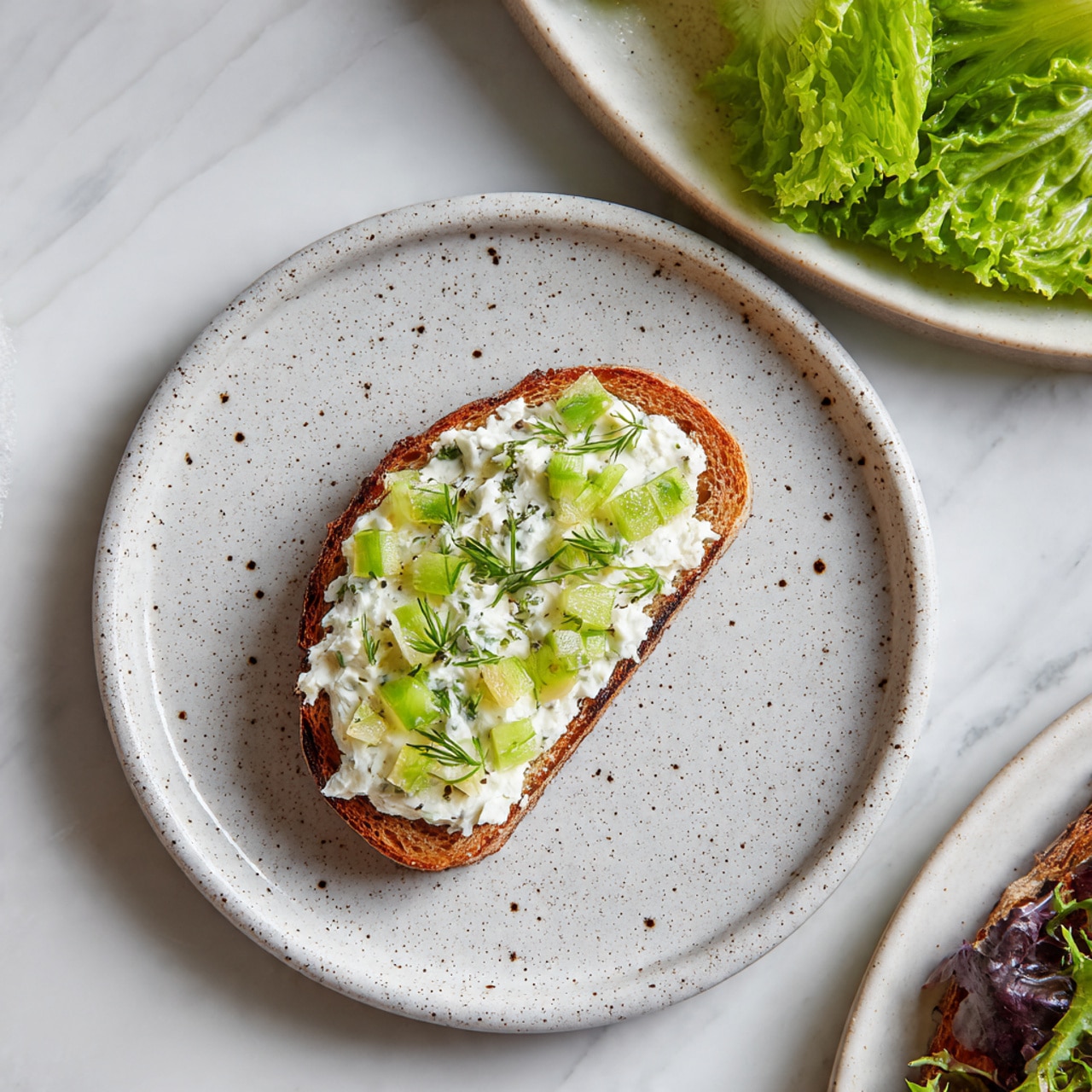 The image shows a sandwich cut into three triangular pieces stacked on top of each other on a white plate. Each sandwich layer has two slices of brown whole wheat bread with a creamy white filling in between, mixed with small green bits that look like chopped vegetables or herbs. The bread has a slightly rough texture with visible grains, and the filling looks thick and smooth with some small chunks. The background is a simple white marbled surface. photo taken with an iphone --ar 4:5 --v 7