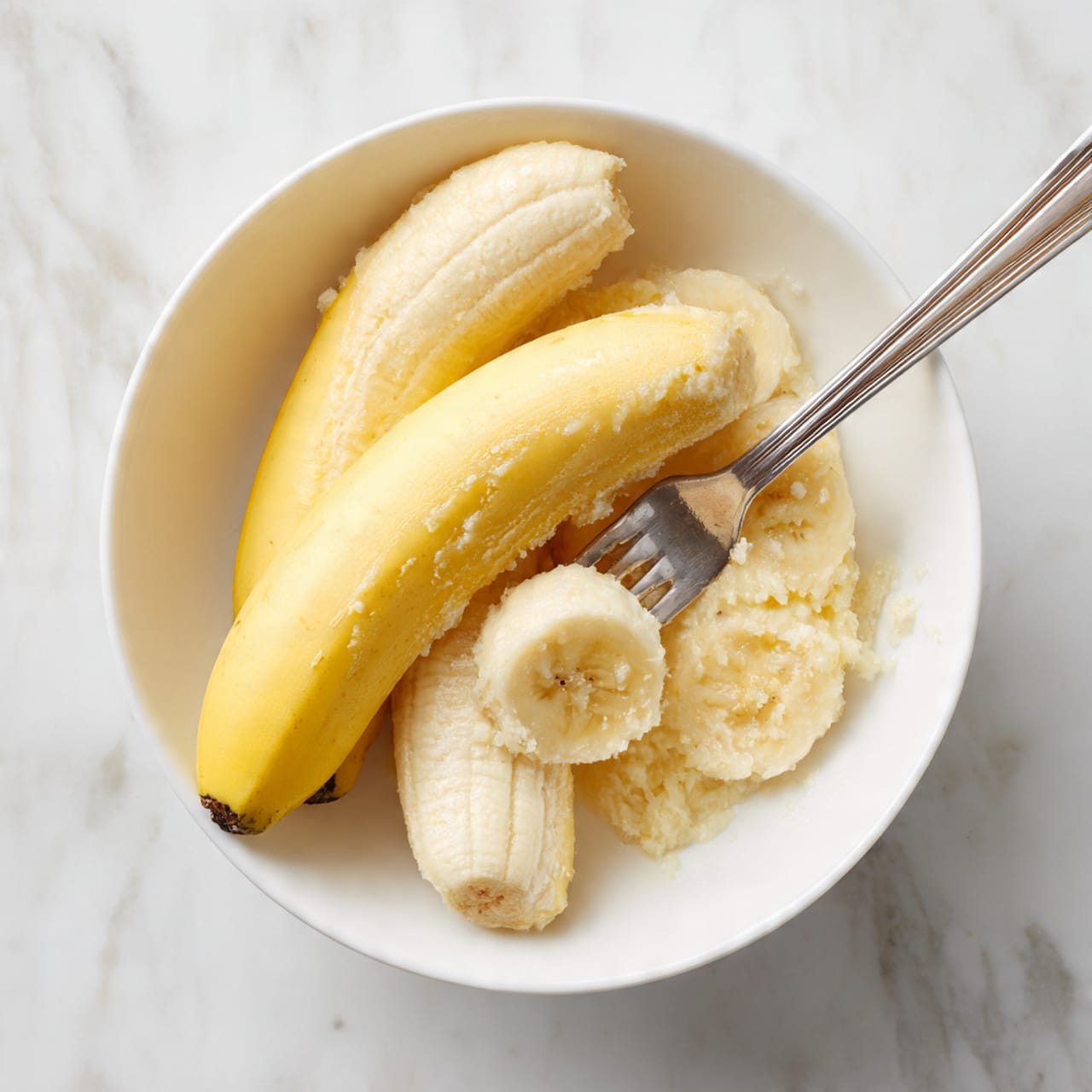 The image shows a rectangular baked loaf topped with many dark chocolate chips spread evenly over the golden-brown, slightly cracked surface. The loaf sits in a white baking pan lined with beige parchment paper that folds over the edges. The texture of the loaf looks soft and crumbly with a few cracks near the center. The background is a white marbled texture with a small round wooden bowl filled with more chocolate chips blurred in the back. Photo taken with an iphone --ar 4:5 --v 7