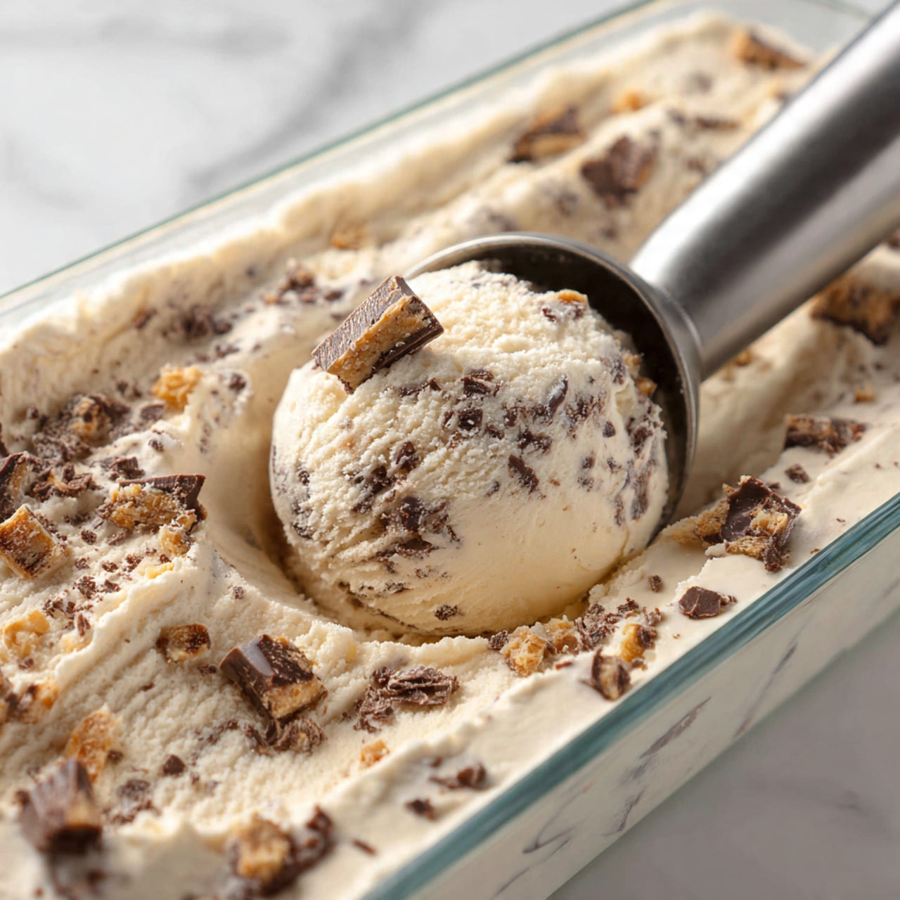 A close-up image shows two scoops of creamy white ice cream with visible bits of caramel or toffee mixed in, stacked perfectly on top of each other. The ice cream is melting slightly, with drips running down the sides of the light brown waffle cone. The cone has a detailed grid pattern and is held by a woman’s hand with a light skin tone. The background is a soft, blurred blue with some white spots, giving a calm and refreshing feel. photo taken with an iphone --ar 4:5 --v 7