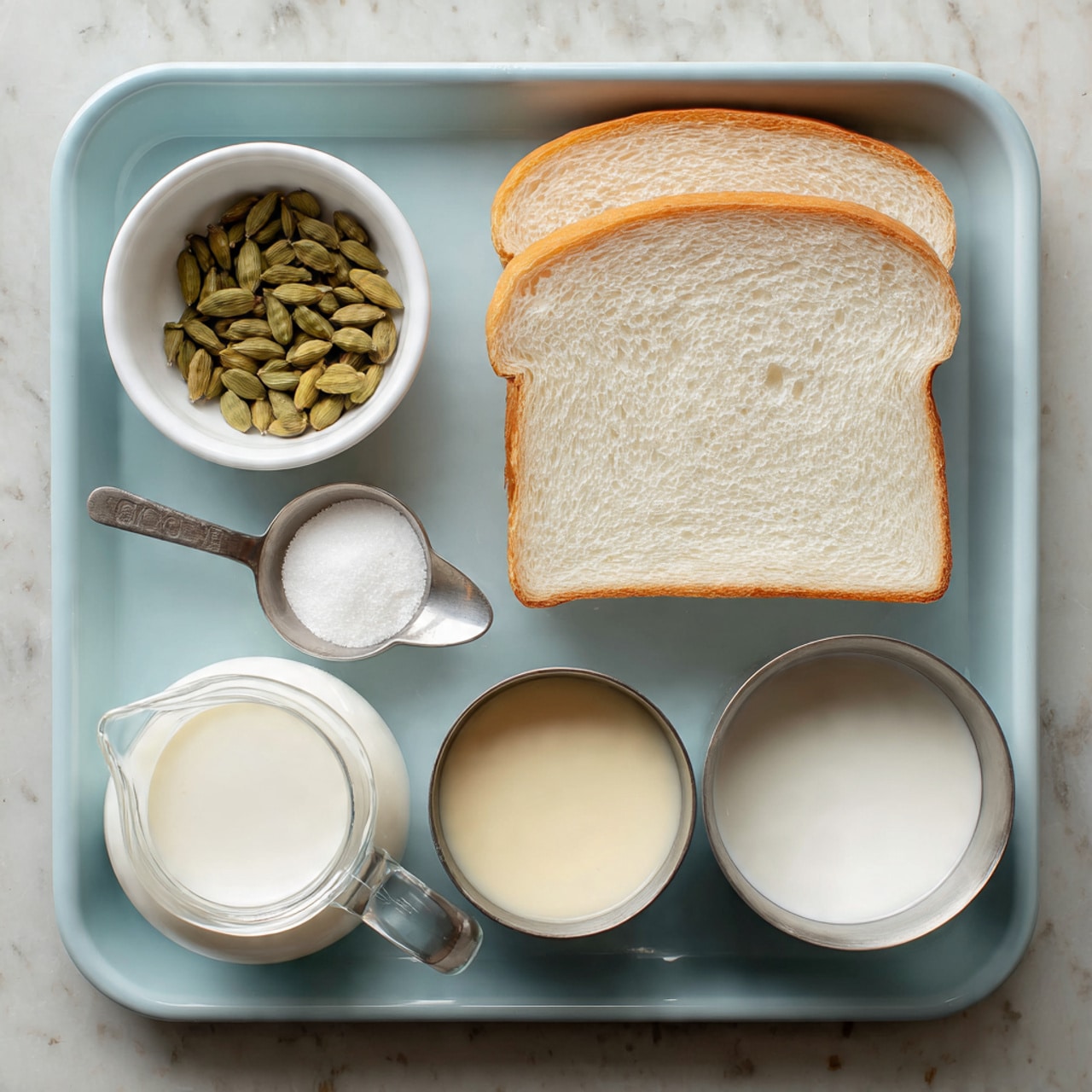 The image shows a light blue tray with different ingredients neatly placed on it. At the top right, there are two slices of white bread stacked slightly on each other. On the top left, there is a small white bowl filled with green cardamom pods. In the bottom half of the tray, from left to right, there is a small clear glass pitcher filled with white milk, next to it a small silver bowl filled with cream-colored condensed milk. To the right of the silver bowl, there is a round metal cup holding white milk that is partially covered by a woman’s hand holding a small metal spoon. The tray sits on a white marbled surface. photo taken with an iphone --ar 4:5 --v 7