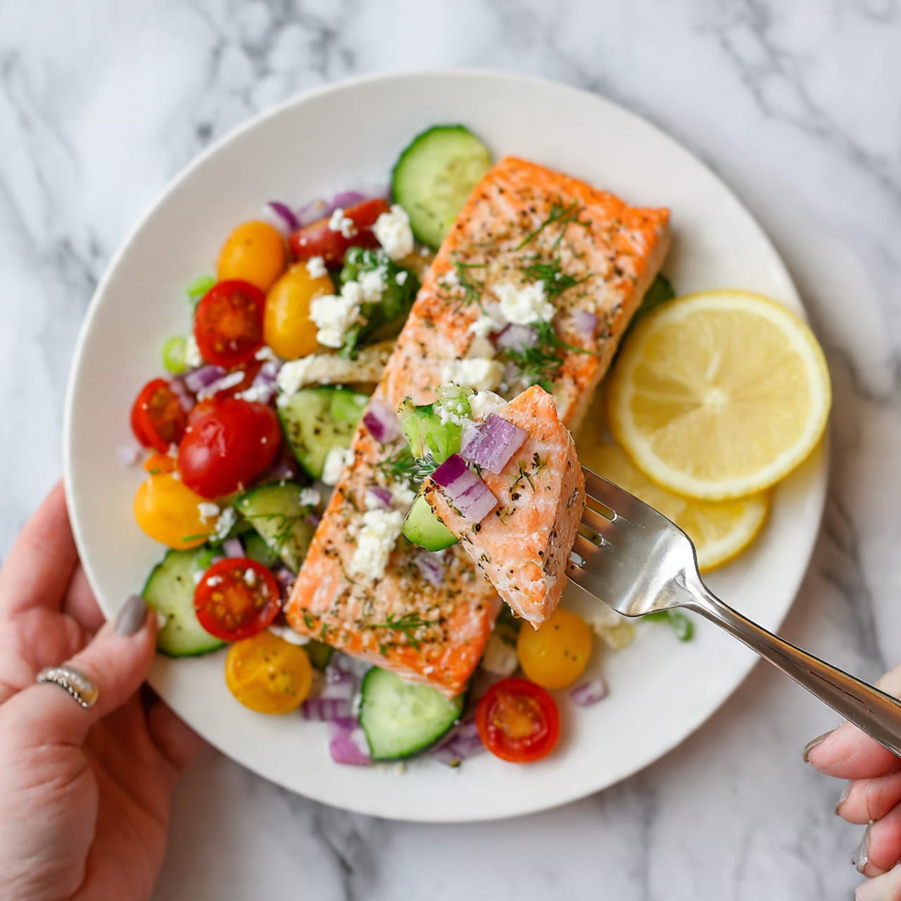 The dish shows three pieces of cooked salmon fillets with a light pink color and a sprinkling of black pepper on top. On top of each fillet, there is a fresh salad made of yellow and red cherry tomatoes, small white cheese pieces, chopped cucumber, green onion, red onion, and green leafy herbs. At the bottom right of the plate, there are three thin yellow lemon slices. All the food is arranged on a white plate with a blue rim, set on a white marbled textured surface. Photo taken with an iphone --ar 4:5 --v 7