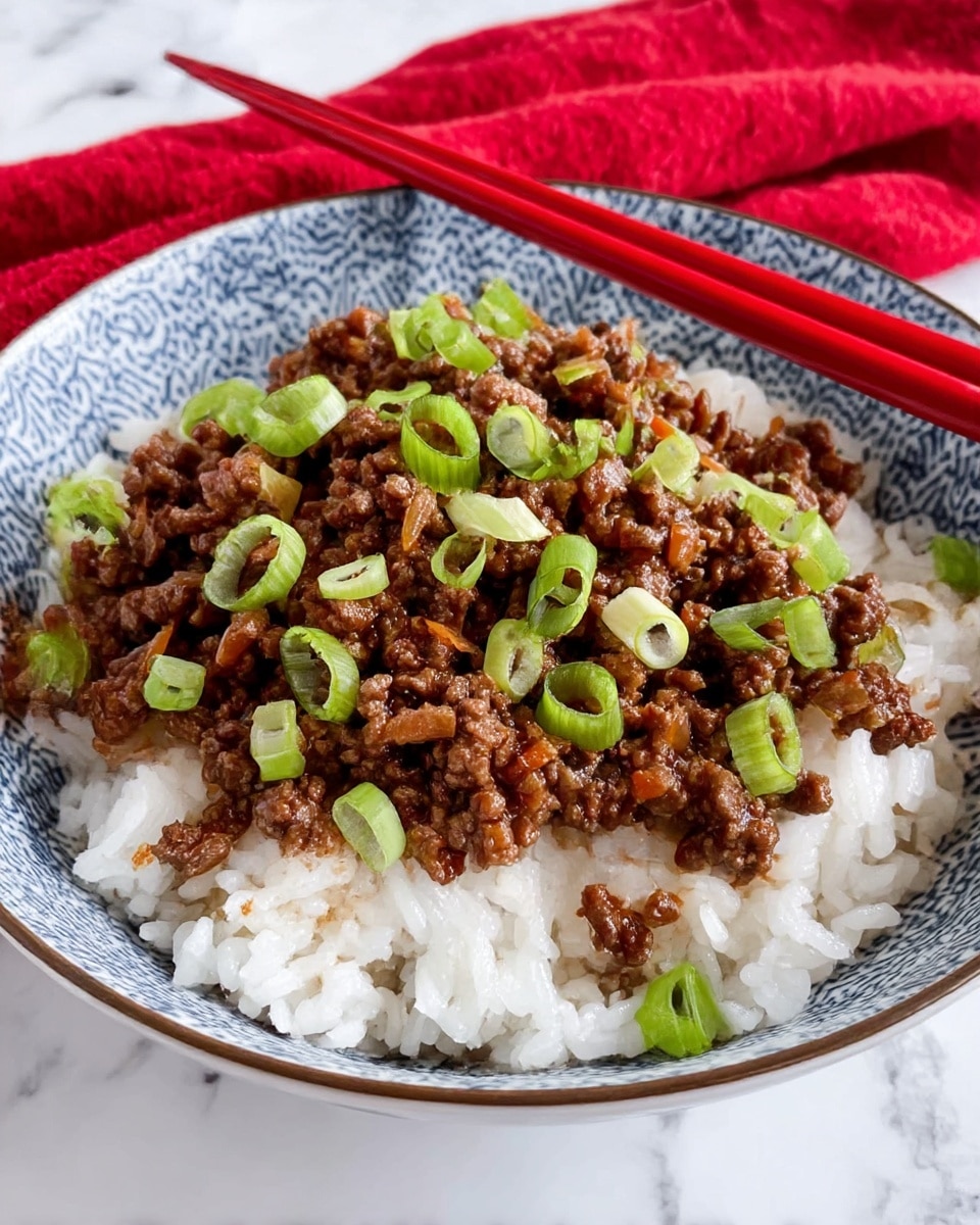 A white bowl with a blue pattern holds a dish with one base layer of white rice, fluffy and spread around the edges. On top is a second layer of cooked ground meat mixed with small bits of orange vegetables, rich dark brown in color with a glossy look. The dish is garnished with small bright green round slices of green onions scattered over the meat. Red chopsticks rest on the top edge of the bowl with a red cloth in the background on a white marbled surface photo taken with an iphone --ar 4:5 --v 7