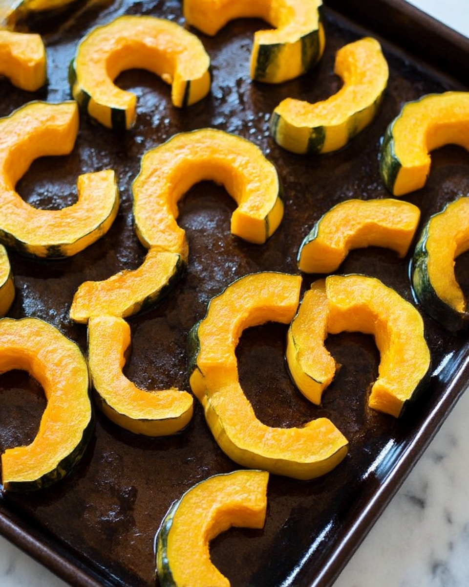 A white plate holds several roasted orange slices of delicata squash arranged in a loose circular pattern, each piece showing caramelized edges with a slightly charred texture. Bright red pomegranate seeds are scattered all over the squash, adding clusters of shiny jewel-like color. Small sprigs of fresh green thyme are placed sparingly on top, creating a fresh contrast. The plate sits on a white marbled background, with two halved pomegranates filled with more seeds positioned at the top edge. A light gray cloth is partially visible at the bottom left corner. Photo taken with an iphone --ar 4:5 --v 7