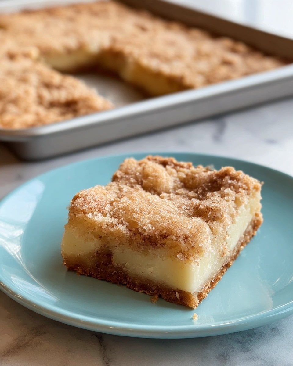 A single square piece of dessert sits near the center of a light blue plate, showing two clear layers: a rough, crumbly, golden brown top layer with a slightly cracked texture, and beneath it, a pale, smooth, creamy layer. The bottom layer has an off-white cream color with a soft texture visible at the edges. In the blurred background, a large baking tray holds more of the same dessert with a similar golden brown, textured surface. The scene is set on a white marbled surface. photo taken with an iphone --ar 4:5 --v 7