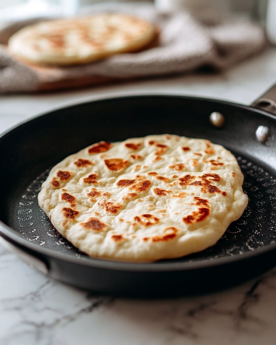 The image shows a large black pan filled with cooked, crumbly reddish-brown ground meat with a wooden spoon resting on the right side and a small green cilantro leaf garnish on top. Below the pan, there is a stack of light beige tortillas with some brown spots on a dark cloth and wooden board. To the left of the pan, several small white bowls hold different toppings: bright green mashed avocado, chopped red onions, and chopped green herbs. There are also two lime wedges and a few loose cilantro leaves scattered around on a dark surface that is replaced with a white marbled texture. Photo taken with an iphone --ar 4:5 --v 7