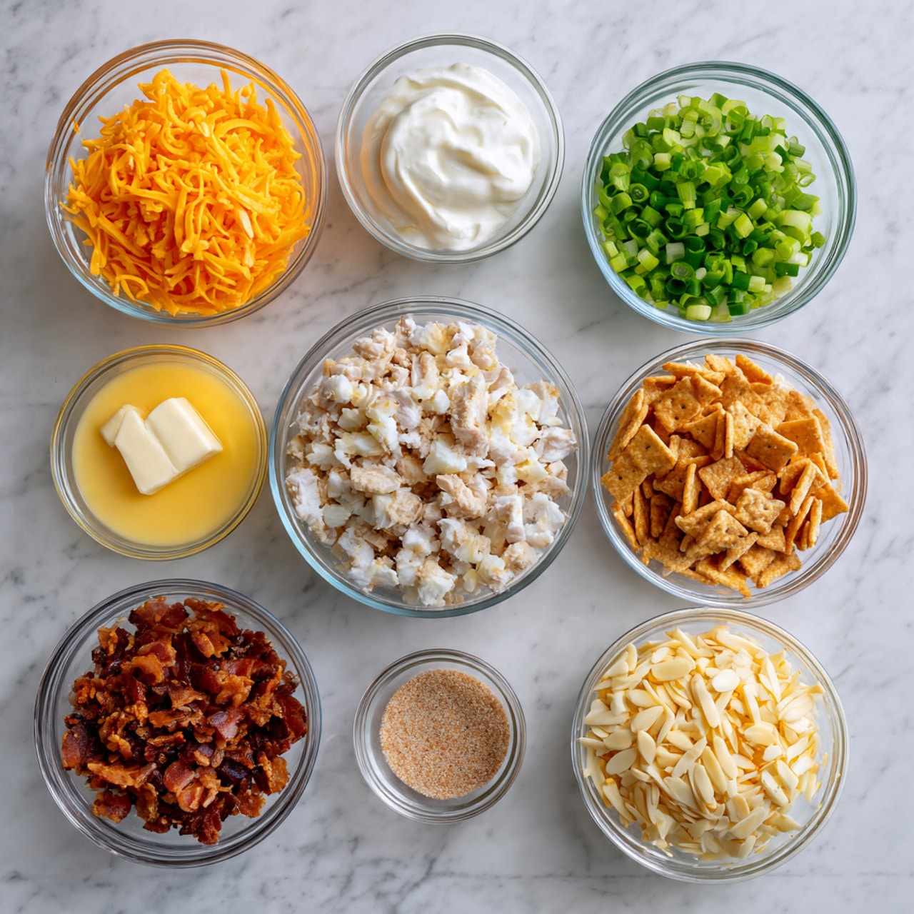 The image shows nine clear glass bowls arranged on a white marbled surface. The top row has three bowls: bright orange shredded cheese in the center, finely chopped green onions on the right, and white creamy sour cream on the left. Below, in the center, there is a larger bowl filled with small pieces of cooked white meat. To the right of this is a bowl with light brown crumbled crackers, and below it is a bowl filled with crispy brown bacon pieces. To the left of the bowl of meat are three smaller bowls: melted yellow butter at the top, yellow cheese sauce in the center, and light beige slivered almonds below. At the bottom right is a tiny bowl with light brown seasoning powder. The overall look is neat and colorful with a white marbled background. photo taken with an iphone --ar 4:5 --v 7