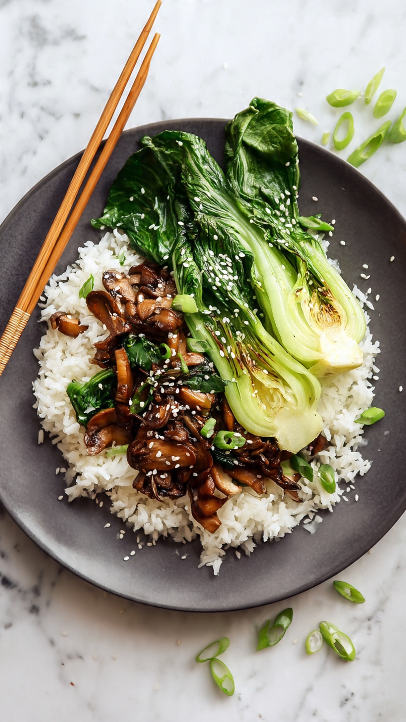 The image shows a white plate with two main sections. On one side, there is a serving of white rice with a few small chopped green onions sprinkled on top. On the other side, there are cooked bok choy leaves and stems, which are bright green with a slightly shiny texture. Mixed in with the bok choy are sliced brown mushrooms, cooked and soft, with a light coating of sauce. Sesame seeds are scattered over the vegetables, adding small white dots for texture. The plate is placed on a white marbled surface with subtle gray veins. photo taken with an iphone --ar 4:5 --v 7