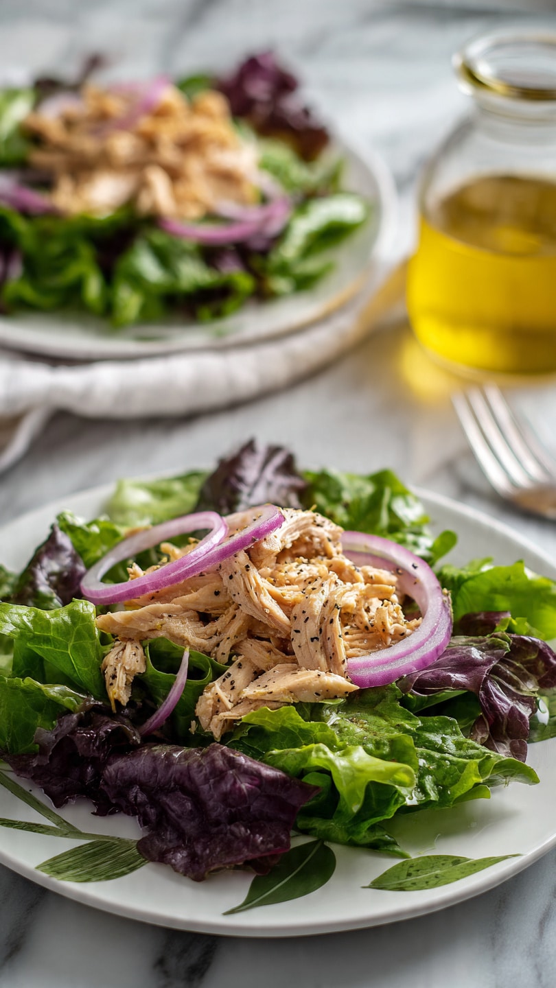 A deep, round, dark blue bowl is filled with shredded light brown chicken pieces, each showing a soft and moist texture with some slight brown seasoning. Behind the bowl on a wooden board sits a white bowl full of mixed green leaf lettuce with red and dark green hues, along with a small round dish of roughly chopped walnuts. Around the bowls are small dishes holding coarse salt and finely ground black pepper, plus a clear glass bottle filled with yellow oil, topped with a stoppers. The whole setup sits on a white marbled surface with part of a floral cloth and golden cutlery visible at the bottom left. Photo taken with an iphone --ar 4:5 --v 7