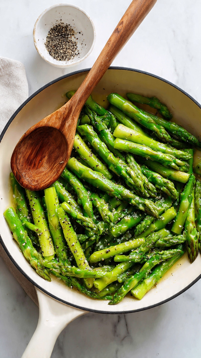 A white oval plate holds a vibrant dish of cooked asparagus stalks arranged in a loose pile, their bright green color and slightly charred texture visible. Scattered over the asparagus are small, uneven pieces of red bell pepper, adding a bright pop of red throughout. White crumbled cheese bits are sprinkled over the top, contrasting with the green and red and adding a soft texture. Small diced white onion pieces and a light sprinkle of cracked black pepper and seasoning flecks dot the dish, creating a mix of colors and textures on the white plate. The plate is set on a white marbled surface. photo taken with an iphone --ar 4:5 --v 7