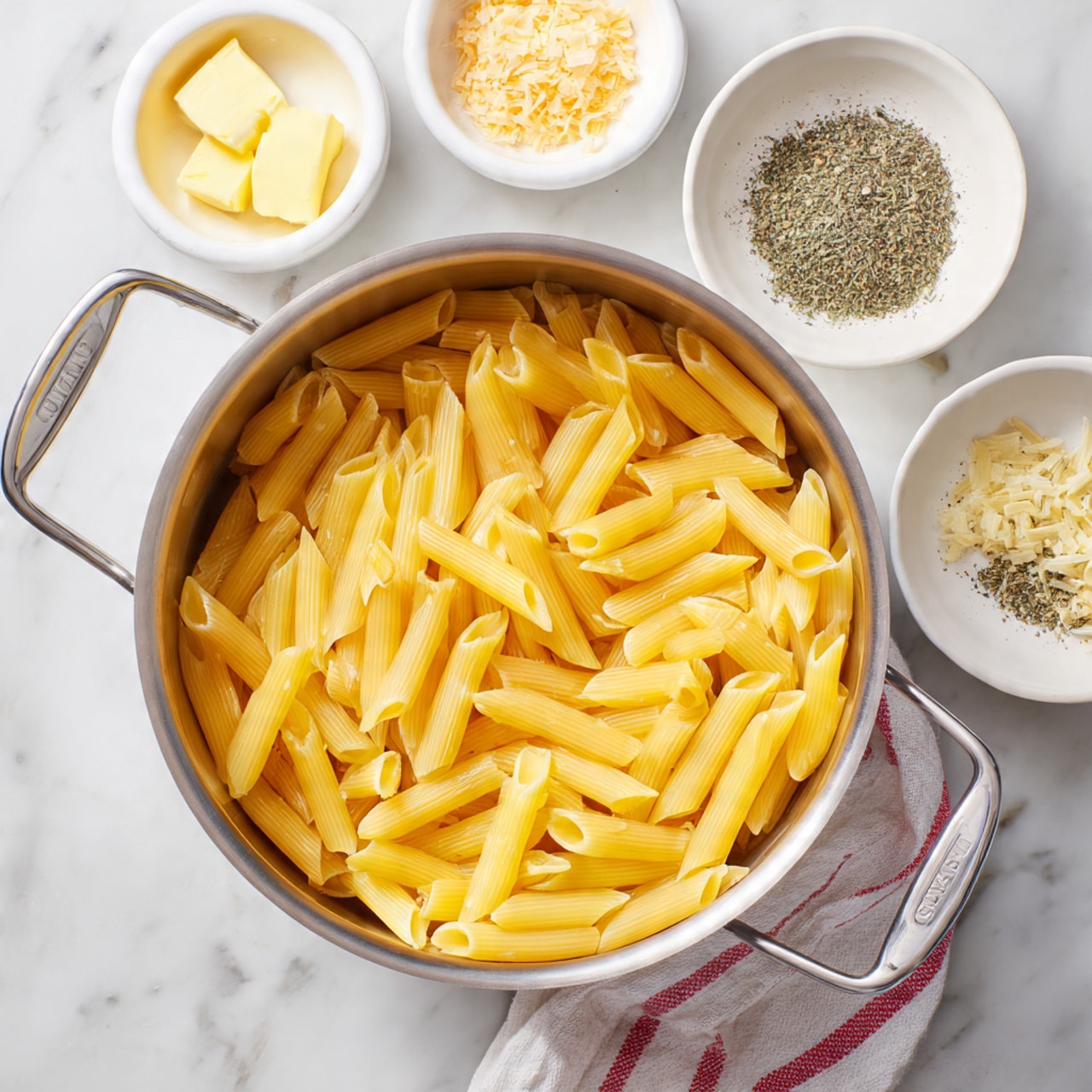 A large pot filled with cooked yellow penne pasta, with each piece smooth and slightly shiny, sits in the center on a white marbled surface. Around the pot are small white bowls holding light yellow butter, minced garlic in a pale orange tone, and small amounts of mixed dried herbs and black pepper, all neatly placed. A white and red striped towel is partially visible under the pot's handles. The scene is bright and clean, focusing on the simple ingredients before cooking. photo taken with an iphone --ar 4:5 --v 7
