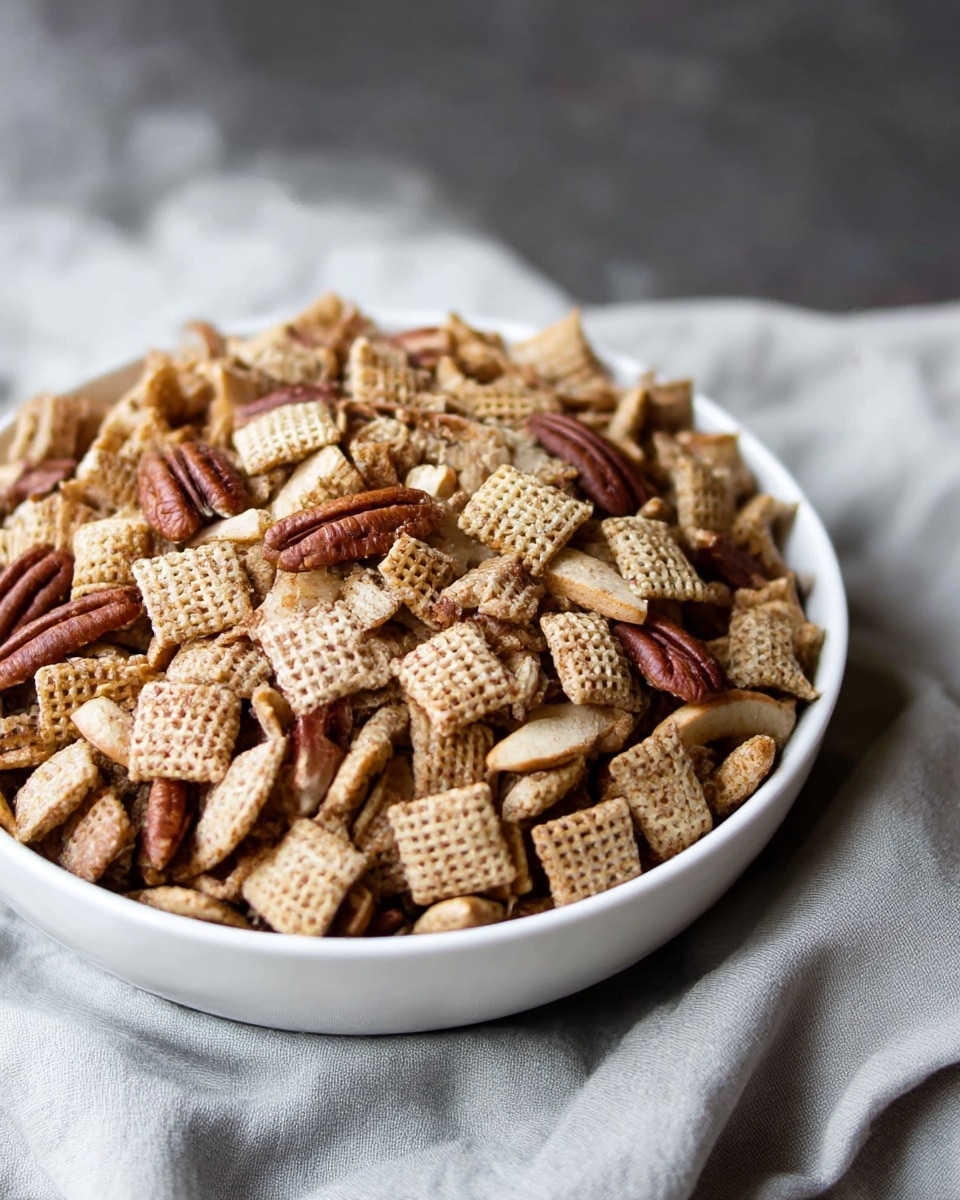 A silver rectangular baking tray filled with a mix of light to medium brown square cereal pieces with a woven texture, scattered with small round white candy-coated pieces, and thin yellowish dried apple chips. On the right side of the tray, there is a wooden spoon resting on top of the mix. The tray is placed on a white marbled surface next to a white cloth with green stripes photo taken with an iphone --ar 4:5 --v 7