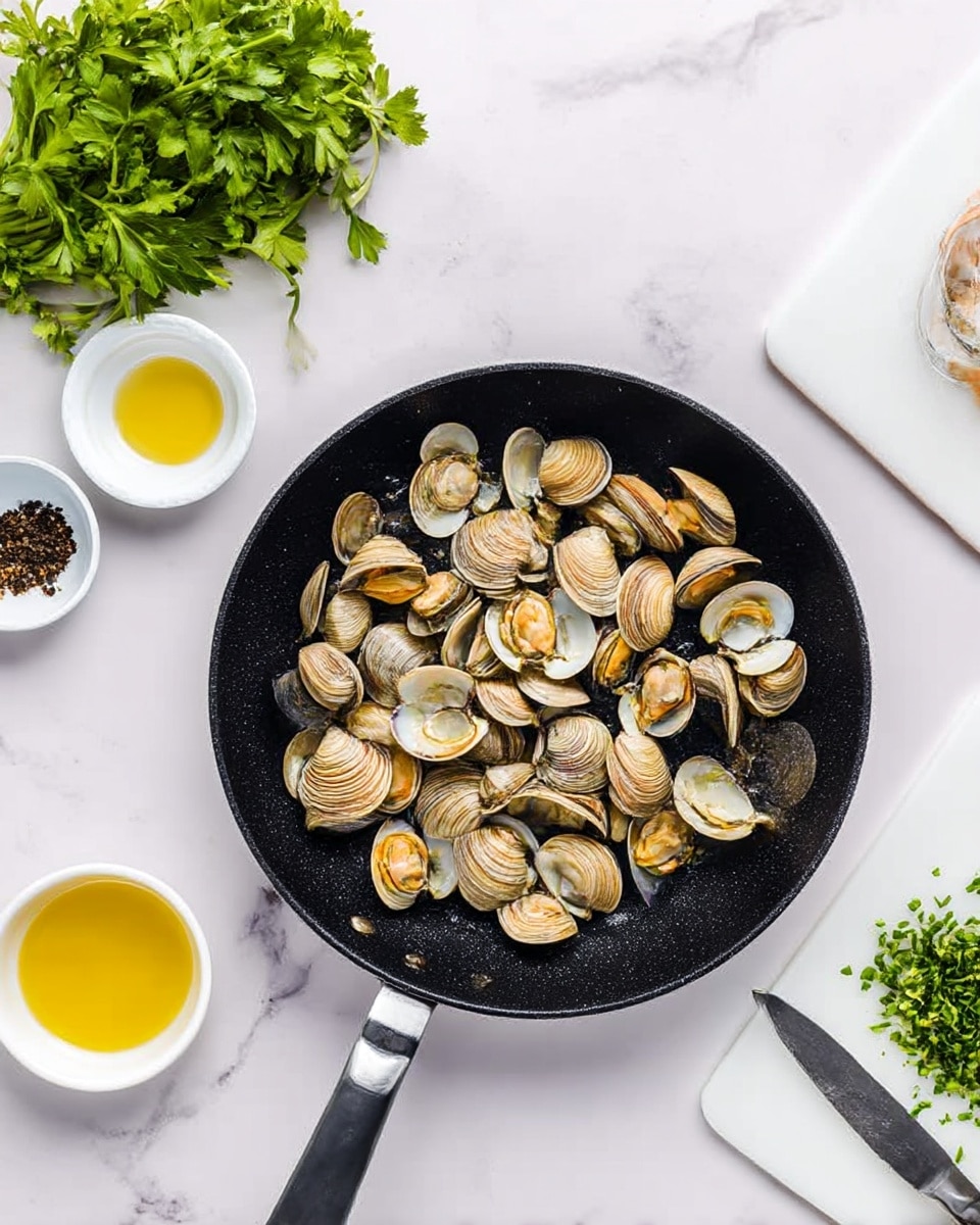 A white bowl with a blue rim holds a neat swirl of yellow spaghetti mixed with small clams, some in their shells, sprinkled with chopped green herbs and a light dusting of black pepper. Above it, a black pan filled with more spaghetti and clams is placed on a round woven mat. To the left of the bowl, two gold forks rest on a gray cloth. The background shows a white marbled surface with small white bowls containing chopped herbs and peppercorns, some loose herbs and peppercorns scattered around, and a bunch of fresh green parsley in the top right corner. photo taken with an iphone --ar 4:5 --v 7