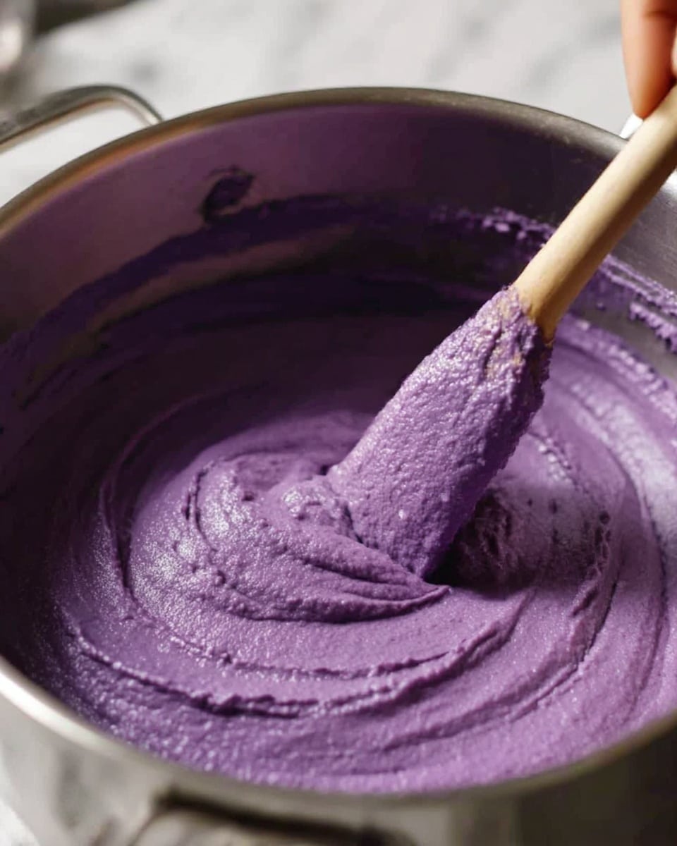 A large white bowl filled with a thick, creamy purple spread that looks smooth with some textured swirls and peaks on the surface. A black-handled knife rests inside the bowl on the right side, partially covered by the spread. The bowl sits on a light wooden surface with a soft white cloth in the background. The texture of the spread is dense but soft, showing small waves and ridges from stirring or spreading photo taken with an iphone --ar 4:5 --v 7