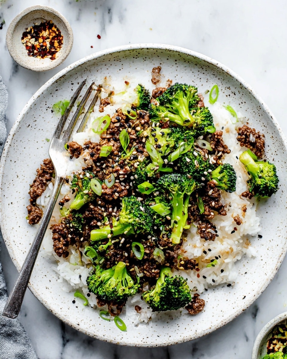 A white speckled plate holds a dish with three clear layers: the bottom layer is white cooked rice with a soft, fluffy texture, the middle layer is bright green broccoli florets with a fresh, slightly crisp look evenly spread on top of the rice, and the top layer is dark brown cooked ground meat scattered throughout and partially mixed with the broccoli. The dish is finished with thinly sliced green onions and black and white sesame seeds sprinkled over, creating small spots of color contrast. A silver fork rests on the left edge of the plate on top of the rice layer, while the background is a white marbled surface with small bowls holding additional seasonings. photo taken with an iphone --ar 4:5 --v 7