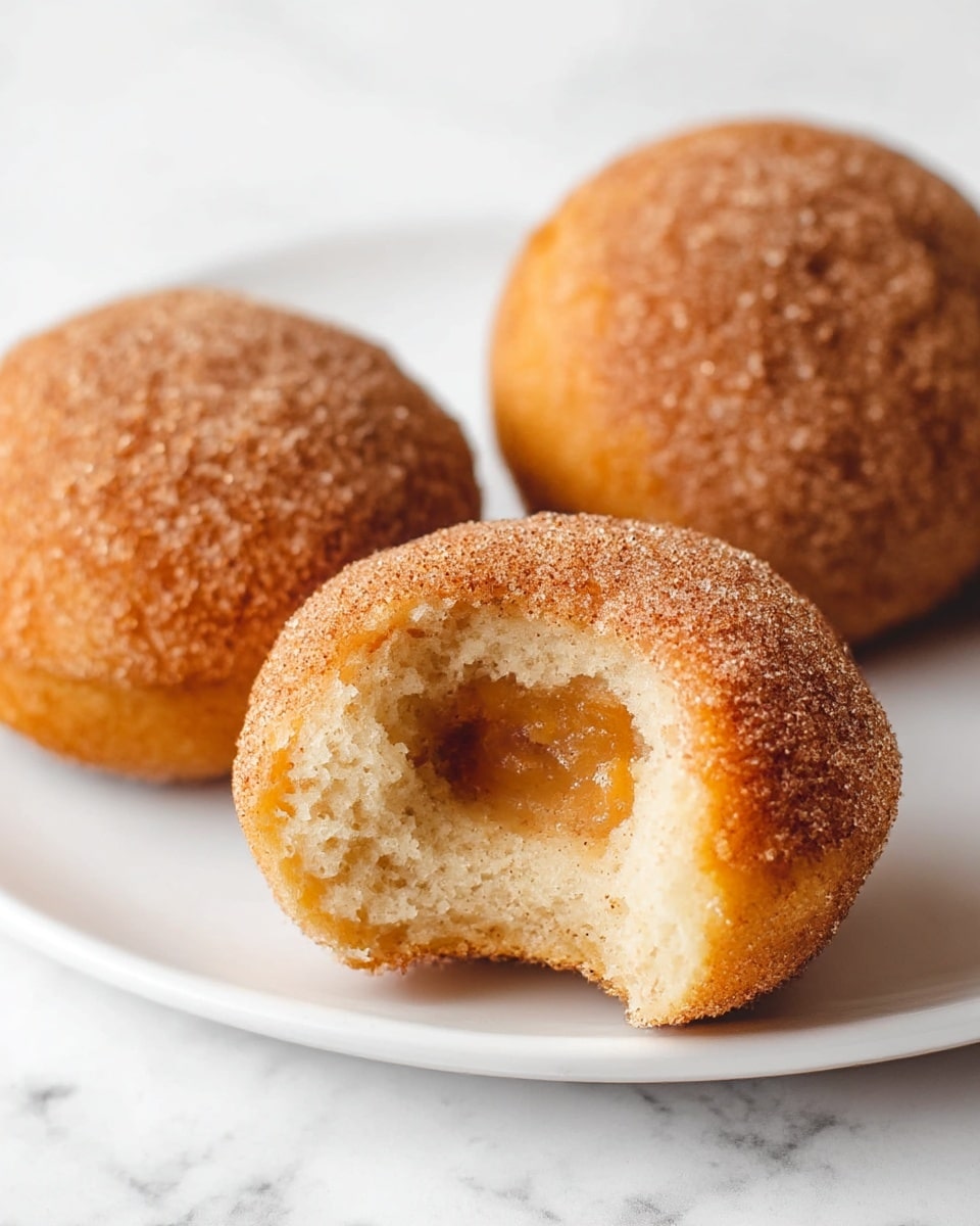 The image shows several round doughnuts stacked closely together, with one on top that has a bite taken out of it, revealing a soft, light yellow inside. Each doughnut is coated with a rough layer of cinnamon sugar giving a sandy texture and light brown color on top, while the sides are a shiny, golden brown. The doughnuts rest on a soft, blue-gray cloth that adds a cozy feel, and the background is a white marbled texture. photo taken with an iphone --ar 4:5 --v 7