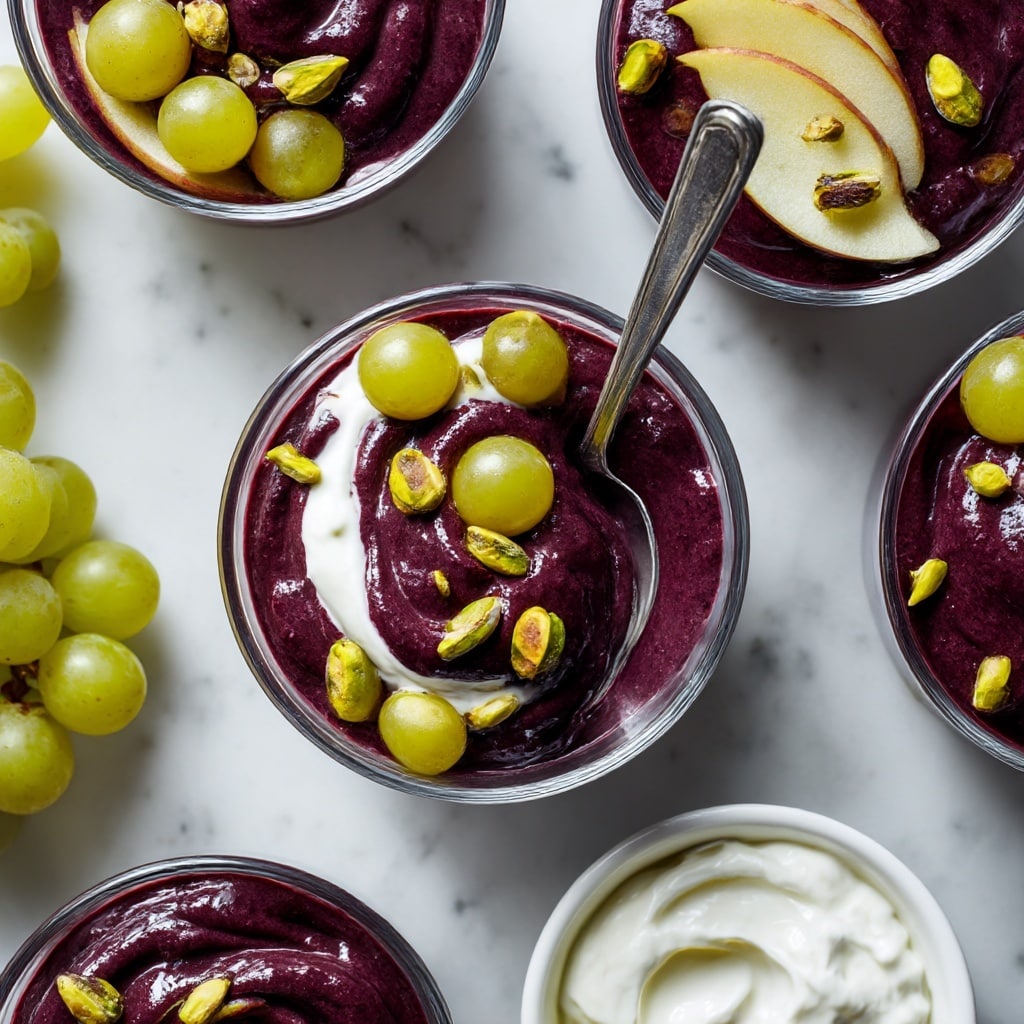 A clear glass bowl filled with thick, smooth purple smoothie. On top, there are four thin slices of apple arranged in a fan shape on the right side. In the center, a dollop of light brown peanut butter with honey drizzled over it. Scattered around and on top of the peanut butter are chunks of walnuts. A silver spoon is placed inside the bowl on the right side. The bowl sits on a white marbled surface with a red apple on the bottom left and a sweet potato on the top left. Photo taken with an iphone --ar 4:5 --v 7