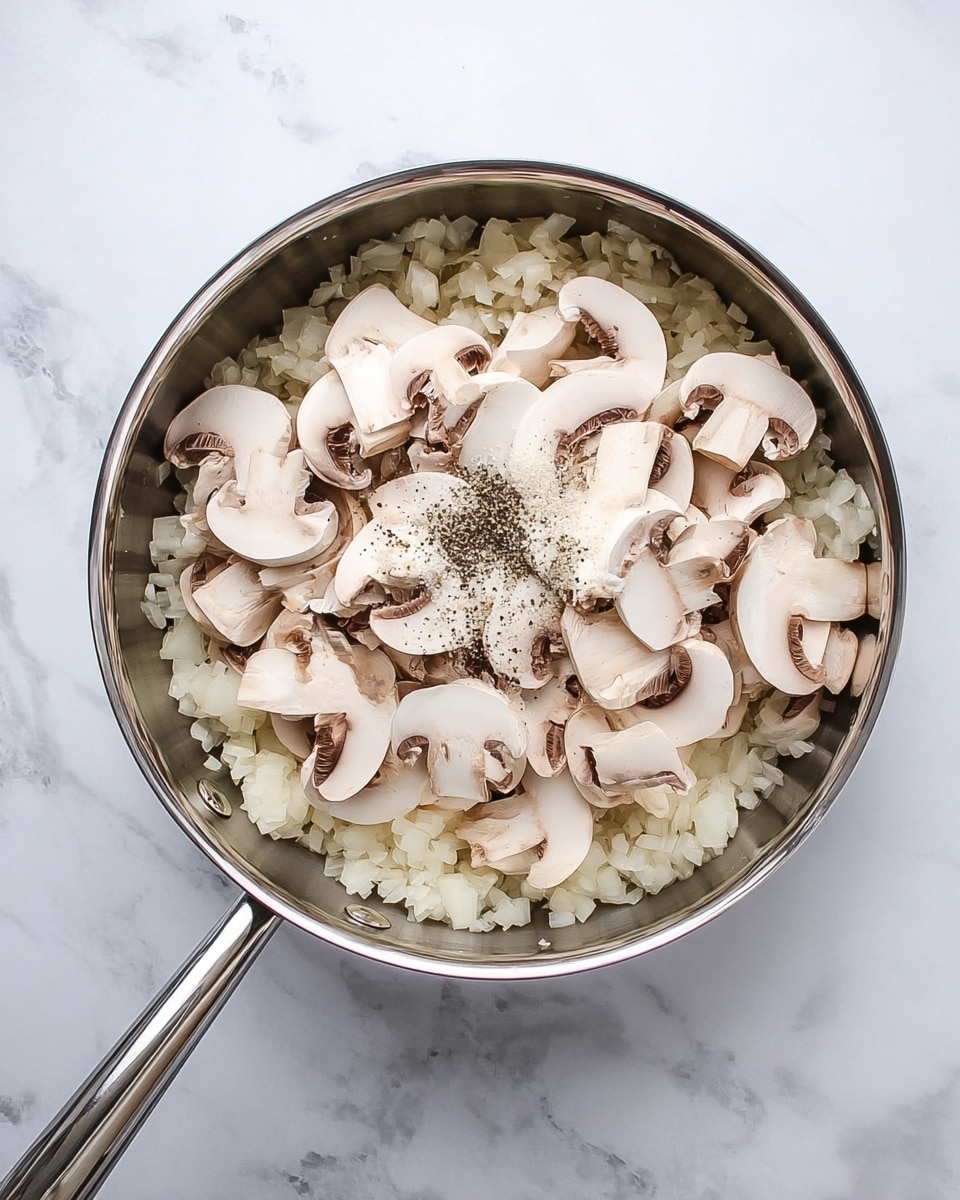 A stainless steel pan sits on a white marbled surface, filled with two layers of ingredients. The bottom layer is a bed of small, chopped white onions, while the top layer is made of sliced white mushrooms scattered unevenly over the onions. There is a small pile of white salt and black pepper sprinkled on top of the mushrooms, adding contrast to the softly textured vegetables. The shiny pan handle extends out to the left side, completing the simple kitchen scene photo taken with an iphone --ar 4:5 --v 7