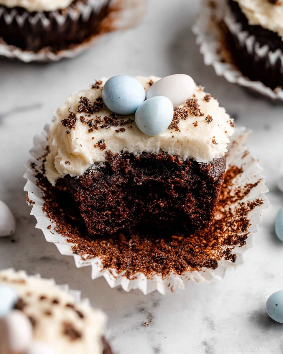 A close-up view of a dark brown cupcake with a white paper liner, topped with a thick layer of white creamy frosting covered in shredded coconut that gives a snowy texture; on top, there are two small pastel-colored candy eggs, one pale pink and one light blue with tiny specks. In the background, there are more similar cupcakes blurred out, all sitting on a black wire cooling rack with a soft pink cloth underneath. A few candy eggs in pastel yellow and pink are placed near the front cupcake on the rack. The backdrop is a white marbled texture. photo taken with an iphone --ar 4:5 --v 7