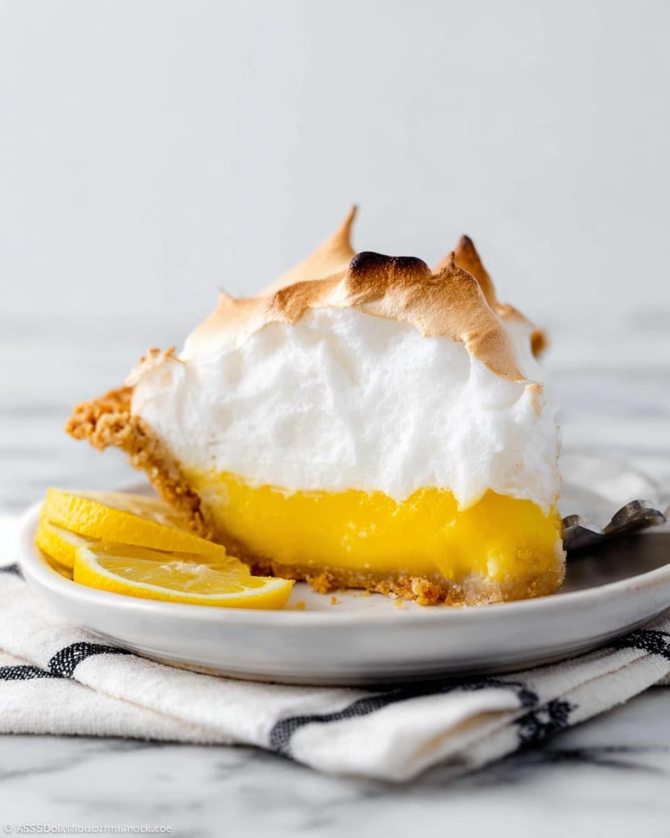 A slice of pie shows three layers on a white plate: the bottom layer is a light golden brown crust with a crumbly texture, the middle layer is a thick, smooth bright yellow lemon filling, and the top layer is a fluffy white meringue with browned peaks, slightly toasted on the edges. Two small lemon slices sit in front of the pie on the plate. The plate rests on a white cloth with black stripes, all set on a white marbled surface. A fork is placed beside the pie slice, partially visible. Photo taken with an iphone --ar 4:5 --v 7