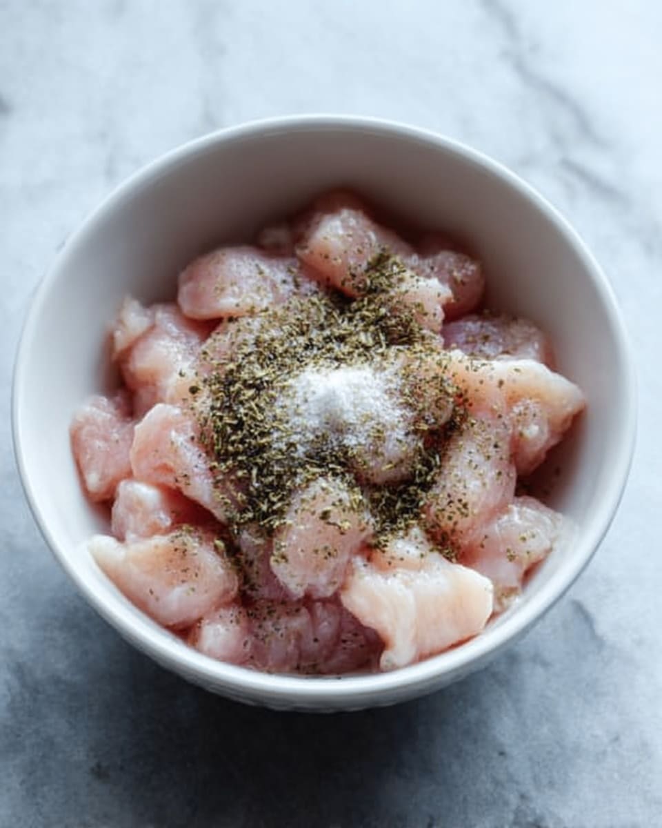 A white plate filled with three layers of cooked rice mixed with small green peas, carrot pieces, chopped onions, and small slices of cooked chicken, all lightly tossed with green herbs scattered on top. The rice looks soft and fluffy with a slight shine. Behind the plate, a black cooking pot with a handle and more rice is slightly out of focus. The surface is white marbled texture, with a blue cloth near the plate and some green herbs in the background. Photo taken with an iphone --ar 4:5 --v 7