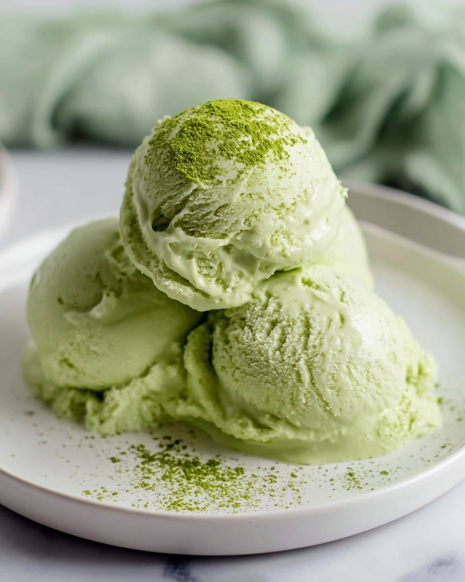 The image shows a close-up of a container filled with pale green ice cream. There are three smooth, round scoops of the ice cream resting inside the container. The texture looks creamy and soft, with slight cracks and small uneven patches on the surface of the scoops. A silver ice cream scoop is partially inside the container, holding one of the scoops, and its metallic surface reflects light. The container is placed on a white marbled surface. photo taken with an iphone --ar 4:5 --v 7