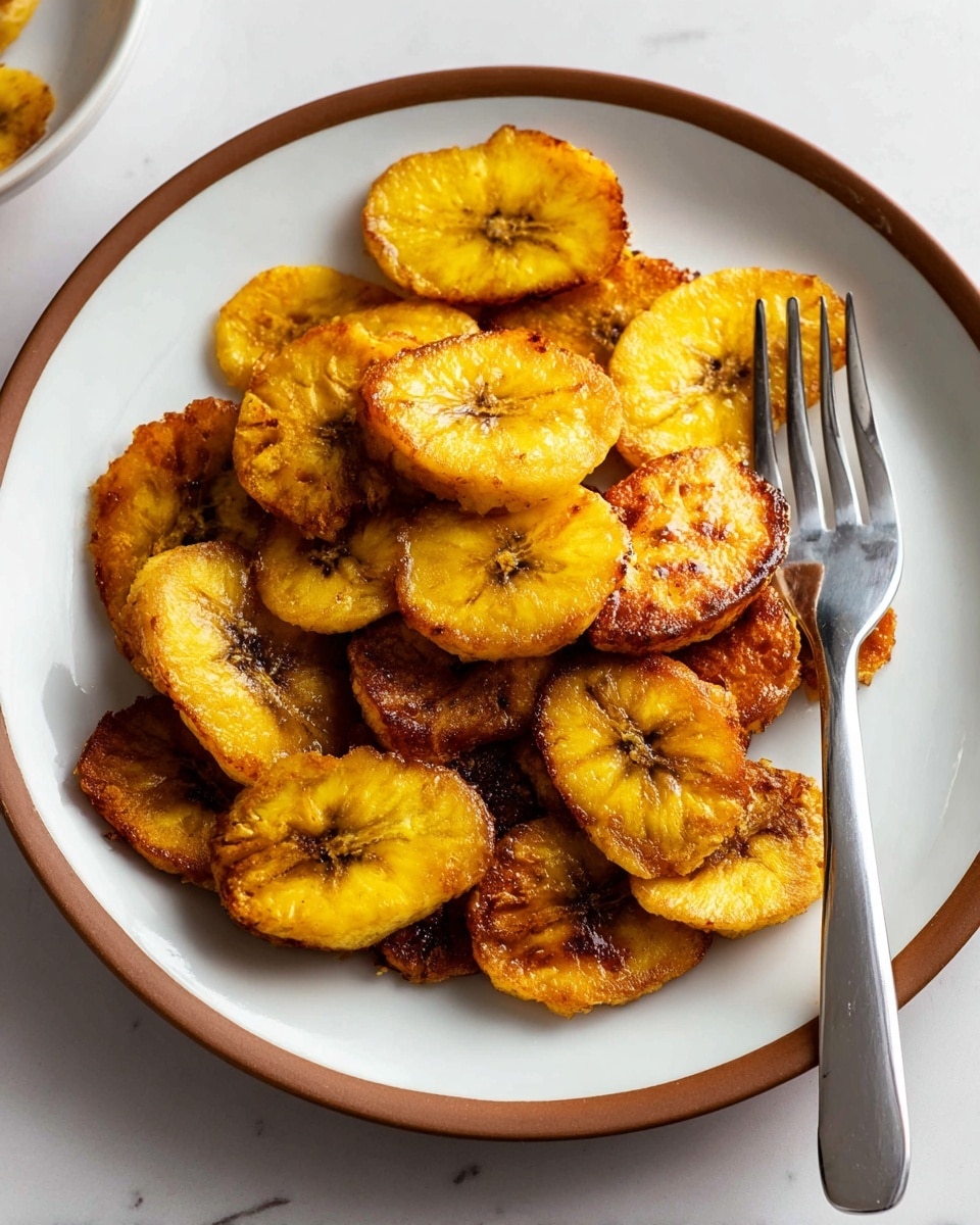 A white plate with a brown rim holds a pile of golden brown fried plantain slices, about two layers thick, each slice showing a crispy texture with some darker browned edges and soft yellow centers. The slices vary in size and shape, arranged loosely in the center of the plate, and a silver fork rests on the right side touching some plantains. The surface beneath is a white marbled texture, bright and clean, with soft natural lighting highlighting the glossy surface of the crisp plantains, photo taken with an iphone --ar 4:5 --v 7