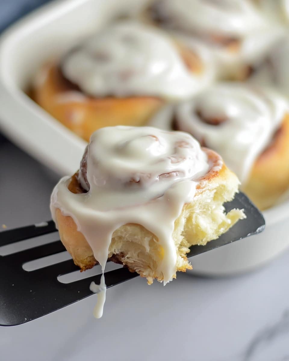 The image shows a round glass dish filled with twelve golden-brown rolls arranged in a circular pattern, each roll displaying a visible spiral of light purple filling inside soft, fluffy dough. The rolls have a slightly shiny crust and look soft and pillowy, with the spirals evenly spaced and uniform in size. The dish is placed on a white marbled surface, with part of a bowl of white frosting and a spatula visible nearby. photo taken with an iphone --ar 4:5 --v 7