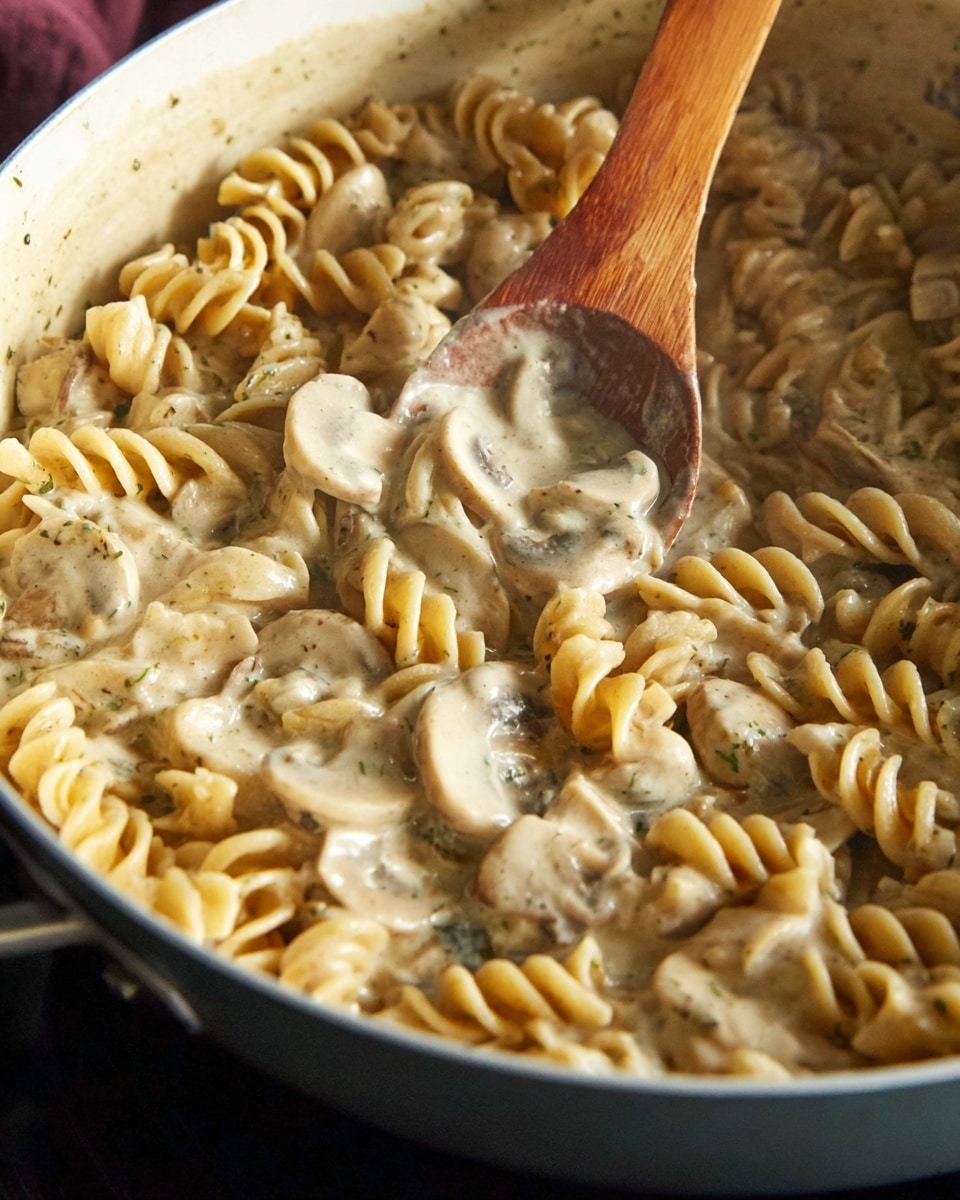 A white plate holds a creamy pasta dish filled with three layers: the base layer is soft, curly yellow egg noodles, the middle layer consists of thick cream sauce with light beige tones, and the top layer shows pieces of light tan cooked chicken and thin, sliced mushrooms with brown edges mixed throughout. The pasta and sauce blend smoothly, and there are small green herbs sprinkled lightly over the dish. The plate sits on a white marbled surface, with a blurred background showing a red and white cloth. photo taken with an iphone --ar 4:5 --v 7
