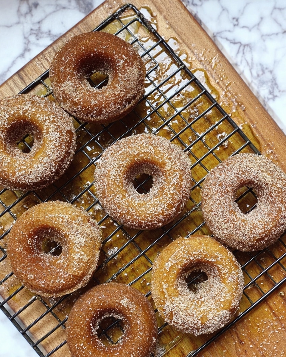 A close-up view of several light brown donuts cooling on a black wire rack over a wooden surface, with five plain donuts on the top rows and three donuts coated in sugar on the bottom right. Below the rack is a round clear bowl filled with a white sugar and cinnamon mix. A woman's hand is holding a sugar-coated donut just above the bowl, showing the coating process. The donuts have a smooth, slightly shiny texture, and the lighting creates a warm, inviting look. photo taken with an iphone --ar 4:5 --v 7
