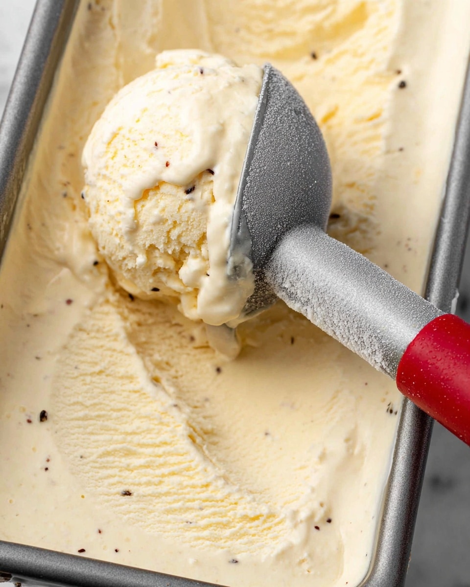 A clear glass bowl filled with five creamy pale yellow ice cream scoops stacked in a pyramid shape. The ice cream has a smooth and slightly textured surface with small dark vanilla specks. The bowl sits on a white scalloped plate, placed on a white marbled surface. In the background, there is a blurred glass bottle and a white and black striped cloth. The lighting is soft and natural, highlighting the texture and color of the ice cream photo taken with an iphone --ar 4:5 --v 7