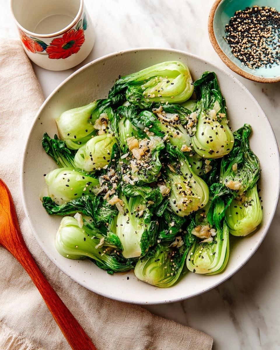 A white bowl holds several layers of cooked baby bok choy with bright green leaves and pale green stems. The bok choy is topped with small pieces of white garlic and sprinkled with a mix of black and white sesame seeds along with some red chili flakes, adding texture and color contrast. Two light brown wooden chopsticks lie against the bowl edge, and a cup with a red floral design is visible in the background, along with part of a pale blue ceramic dish. The surface is a white marbled texture. Photo taken with an iphone --ar 4:5 --v 7