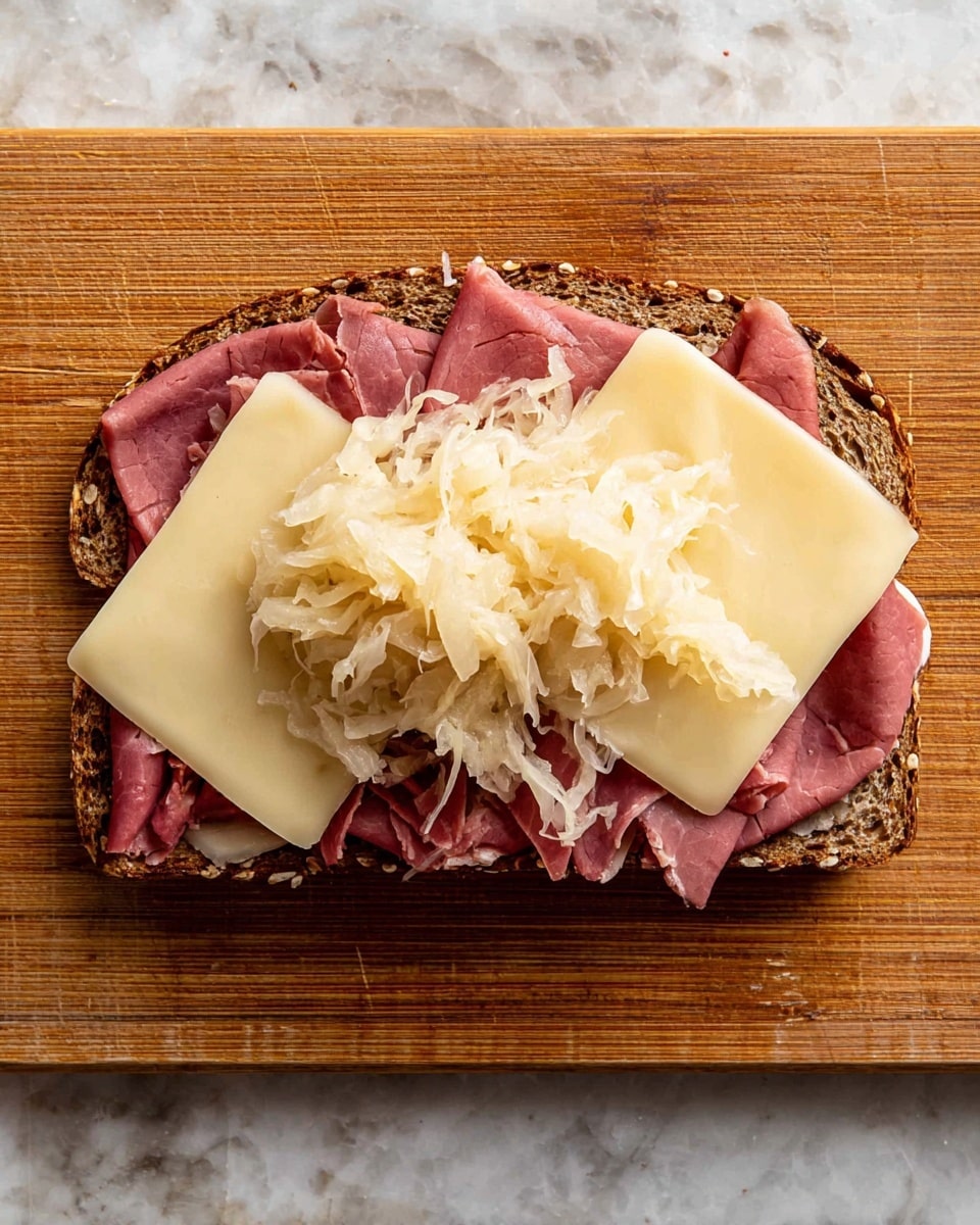 A close-up of a sandwich cut in half showing three main layers inside: the top and bottom slices of toasted rye bread with a dark brown swirled pattern, a thick middle layer of curly, pink sliced meat, and a layer of light yellow melted cheese mixed with light beige sauerkraut on top of the meat. The sandwich sits on a wooden surface with a warm tone, and the textures of the toasted bread with grill marks and the soft, moist meat are clearly visible. photo taken with an iphone --ar 4:5 --v 7