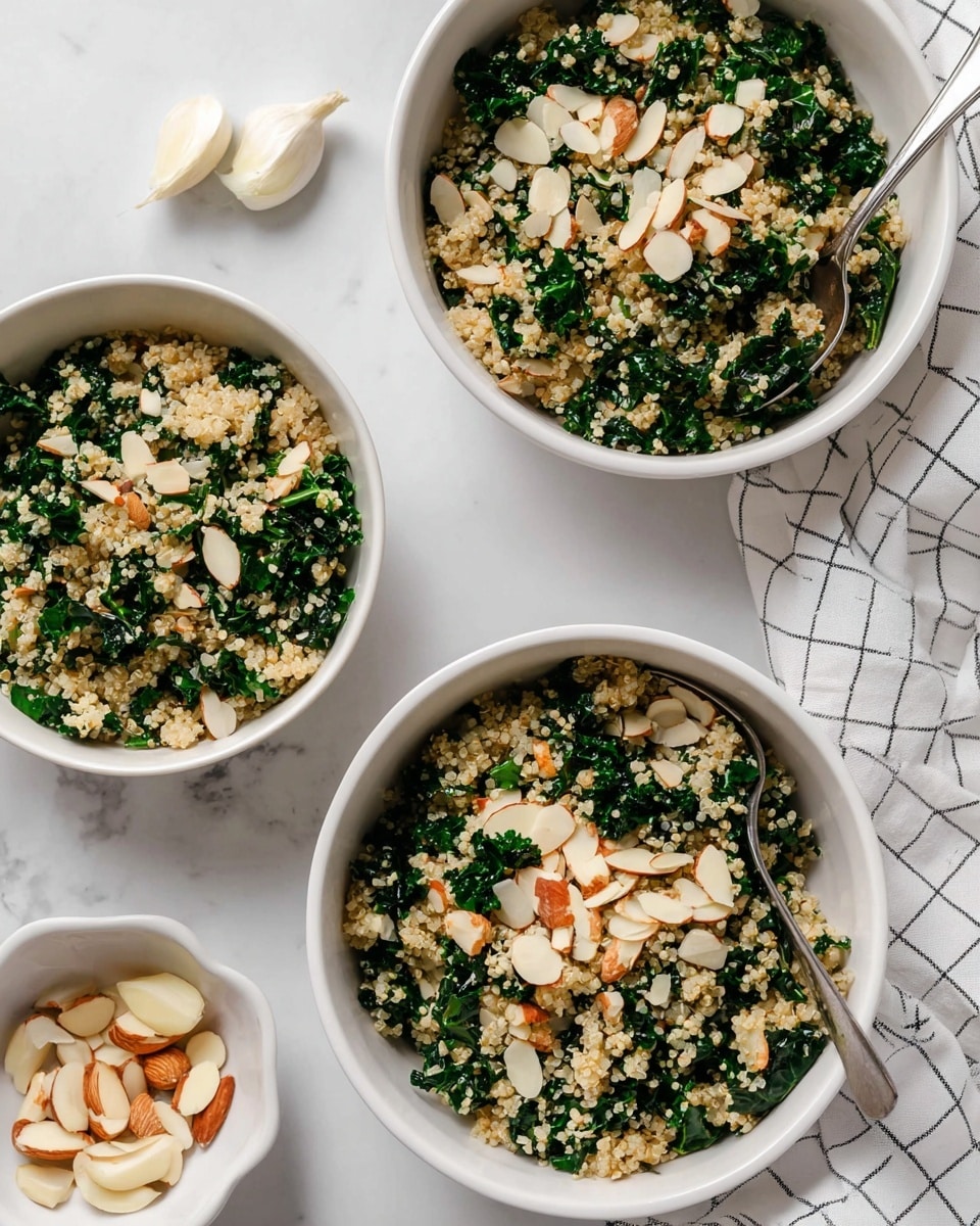 A white scalloped bowl filled with a quinoa salad mixed with bright green chopped kale leaves and scattered thin, light brown almond slices. The quinoa grains are small, pale, and fluffy, mixed evenly throughout the kale. Two black spoons rest inside the bowl, partially sinking into the salad. The bowl is placed on a white marbled surface with a small white bowl of almond slices at the top, and several garlic cloves scattered around. A white cloth with a thin black check pattern lies near the bottom left of the bowl. photo taken with an iphone --ar 4:5 --v 7