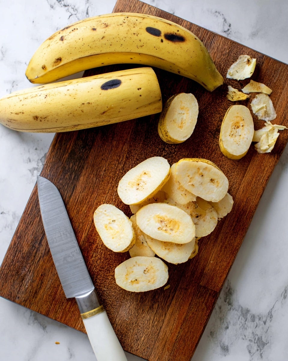 The image shows a wooden cutting board placed on a white marbled surface with two whole yellow plantains with black marks on the top left side. Below the plantains, on the cutting board, are several thick, oval slices of peeled plantain displaying a creamy yellow color with some orange and dark spots in the center. A large knife with a white handle and silver blade lies diagonally across the lower left part of the board. Small pieces of plantain peel are scattered around the cutting board on the marbled surface. photo taken with an iphone --ar 4:5 --v 7