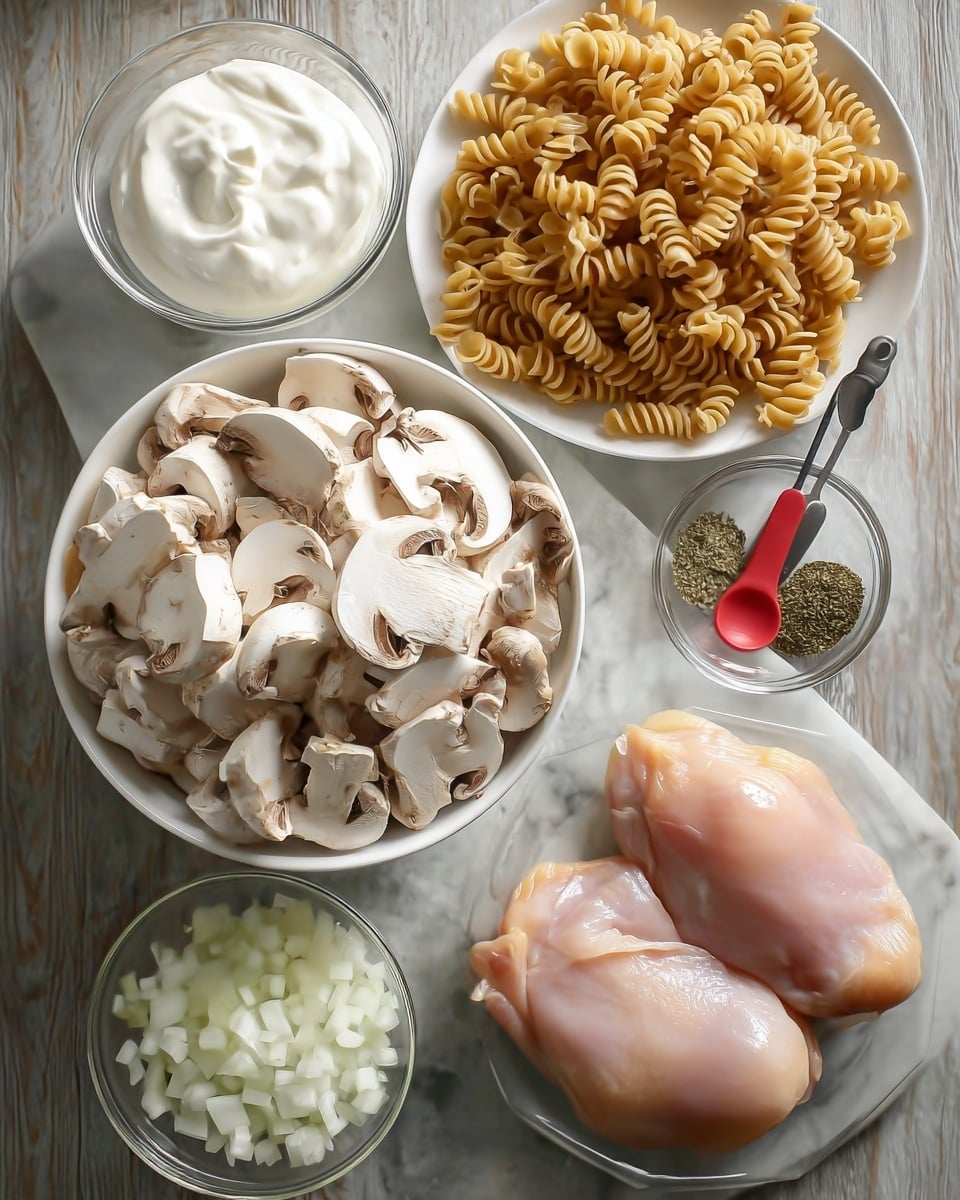 The image shows several bowls and plates with ingredients arranged on a white marbled surface. In the center, there is one white bowl filled with sliced white mushrooms that have brown inner gills. To the top right, there is a white bowl with beige spiral pasta. Below the mushroom bowl, a clear glass plate holds two raw chicken pieces with smooth pale pink skin. To the right of the chicken plate, there is another clear glass plate with chopped white onions in the center and two red measuring spoons, one with green dried herbs and the other with a white powder. At the top left, there is a round white container filled with smooth white sour cream. Photo taken with an iphone --ar 4:5 --v 7